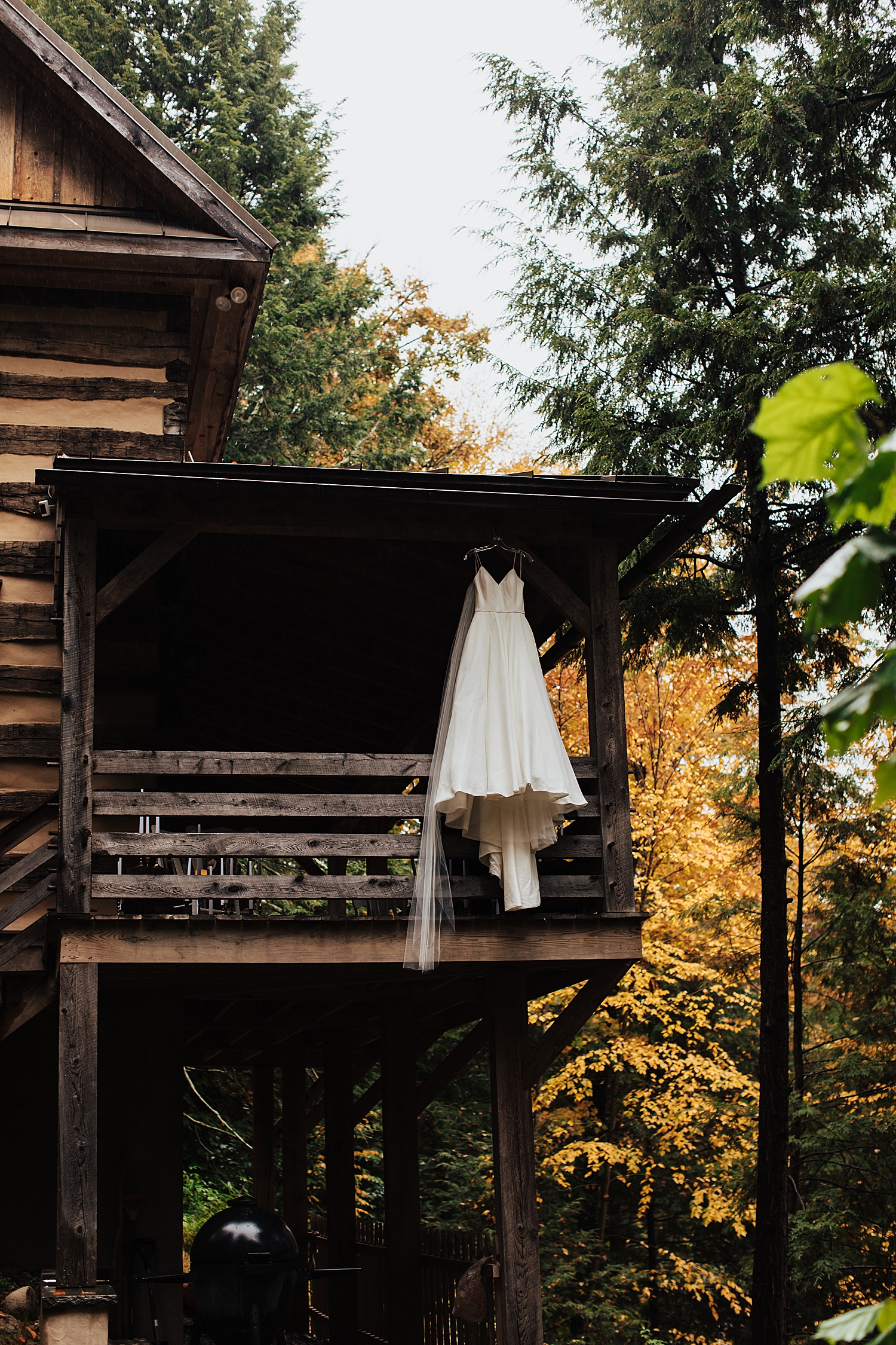 wedding gown hangs off porch of log cabin by Nicole Aston Photography