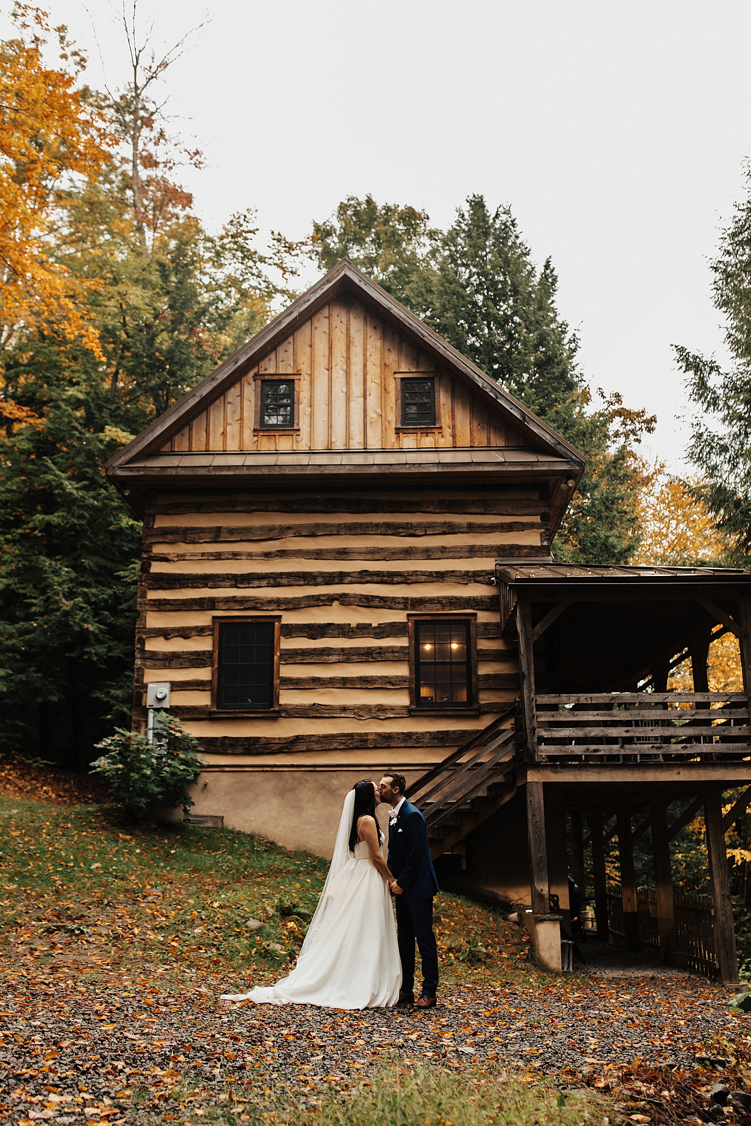 newlyweds kiss in front of big log cabin in Pennsylvania by Nicole Aston Photography