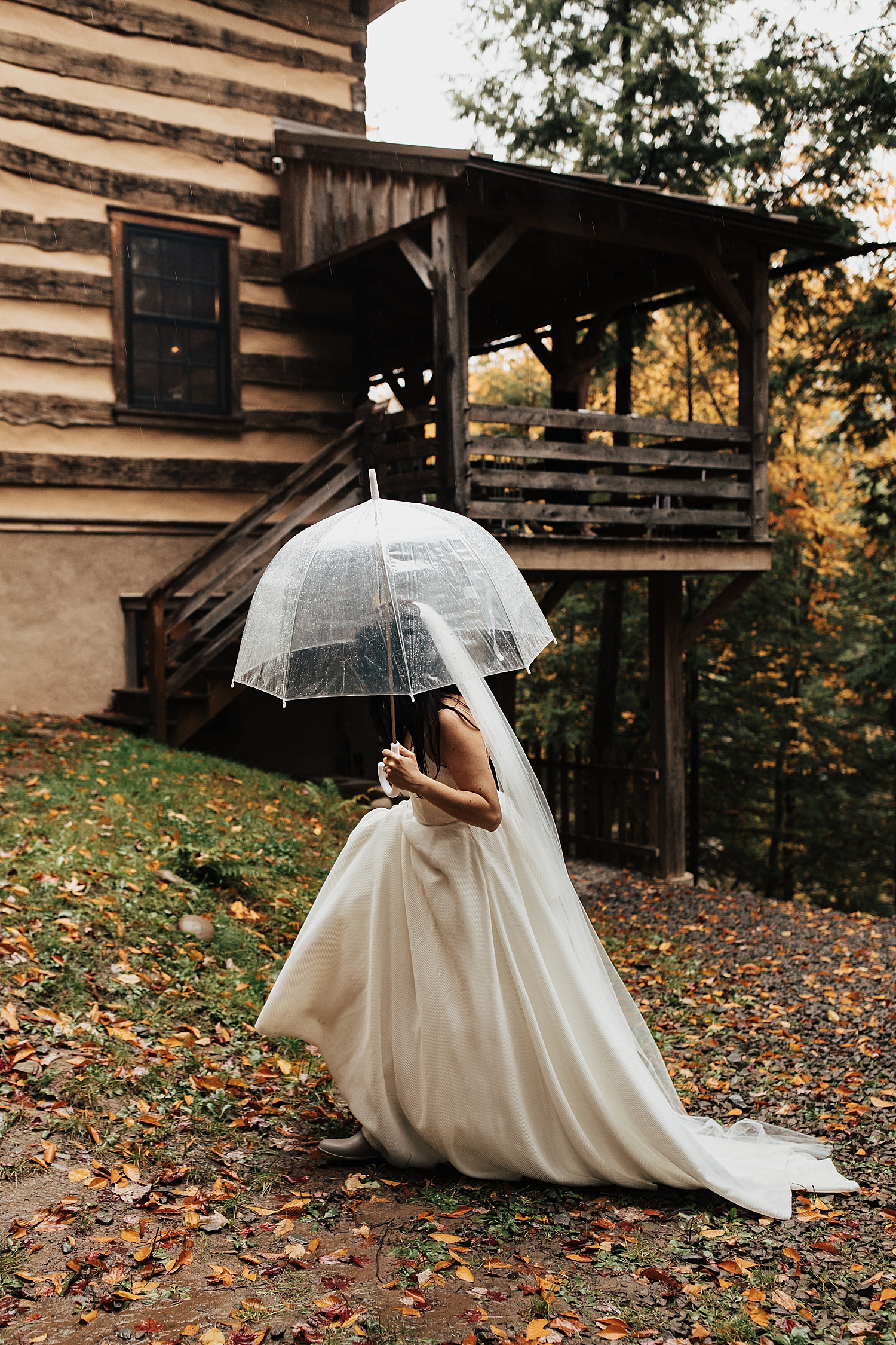 bride walks up hill with clear umbrella for rainy autumnal intimate day