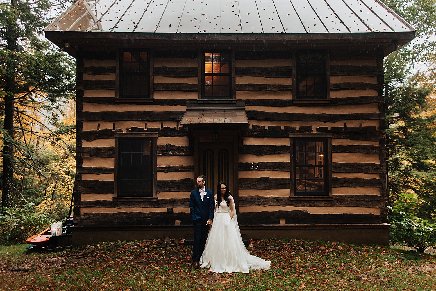 husband and wife stand in front of log cabin in Pennsylvania by Destination wedding photographer