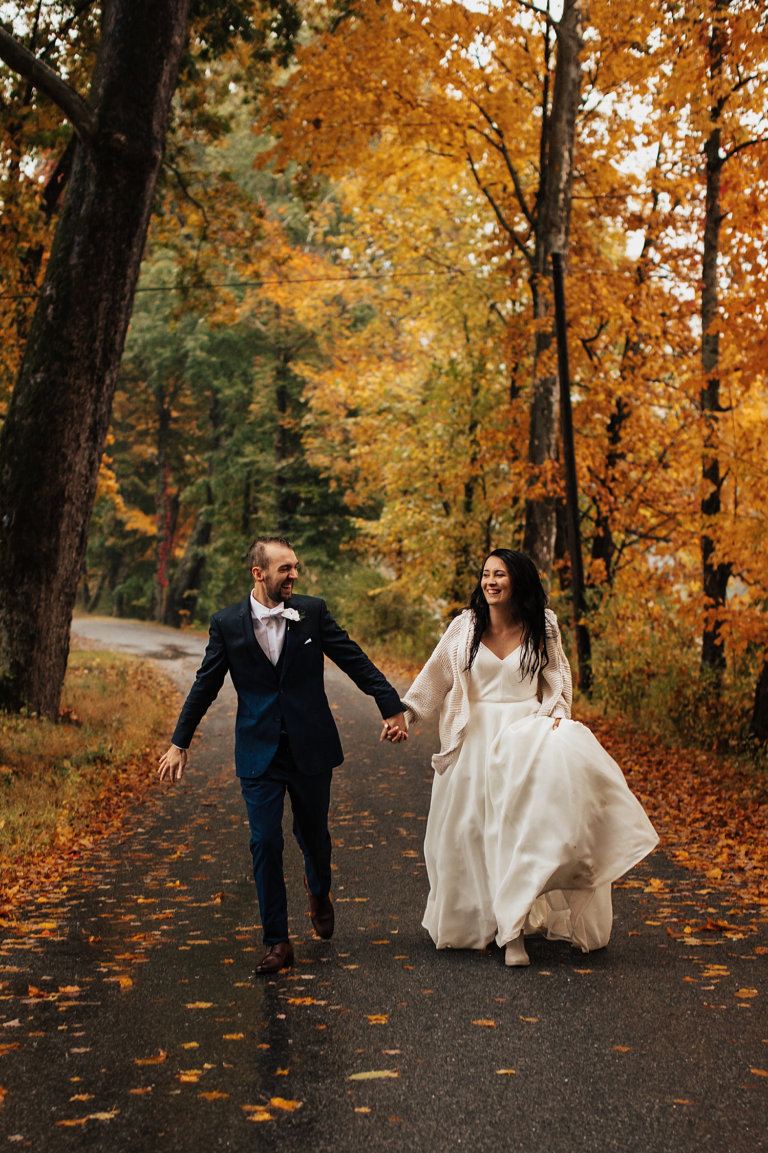 newlyweds run down forest path under orange trees for rainy autumnal intimate day