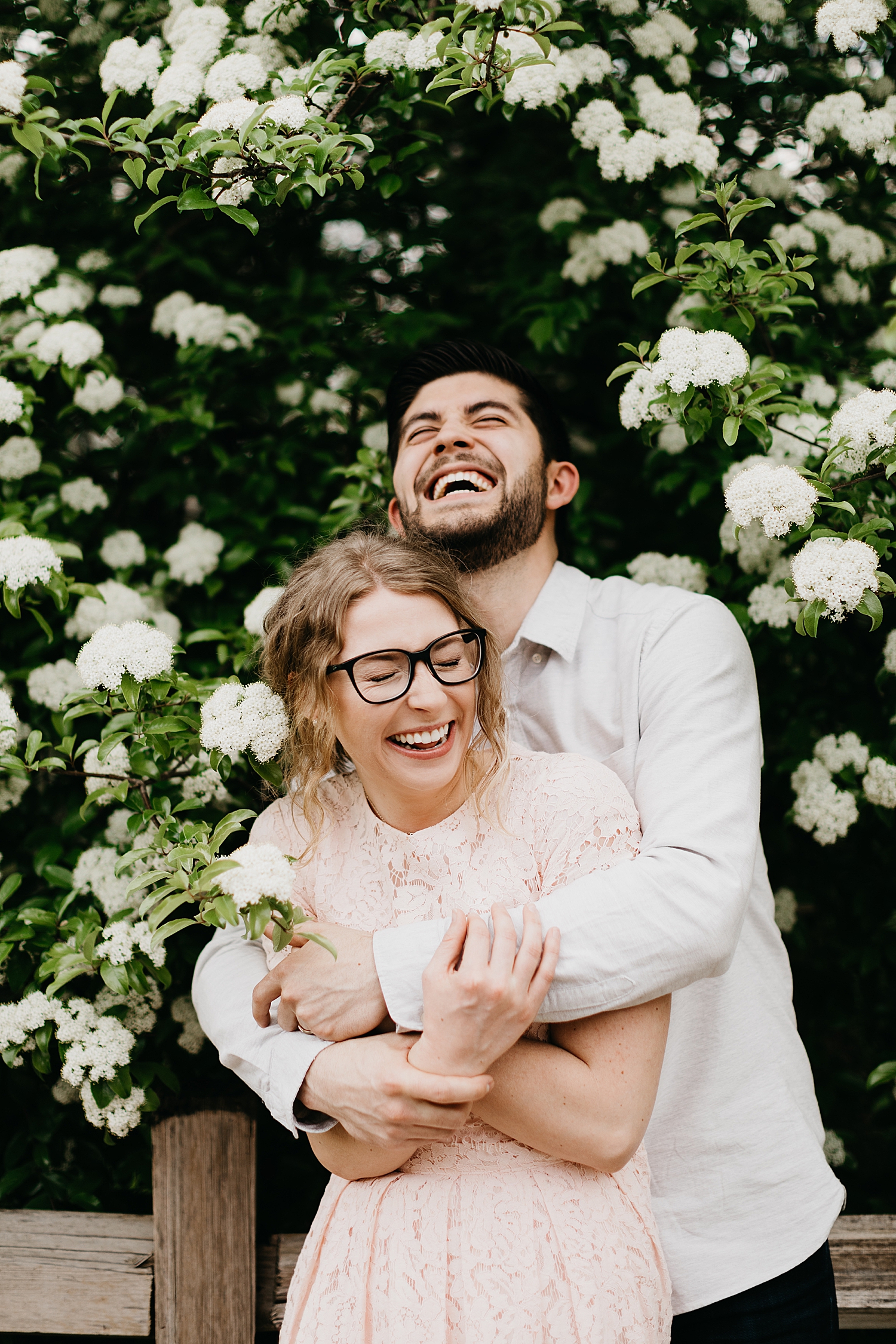 man and wife laugh together under white flowers by Nicole Aston Photography