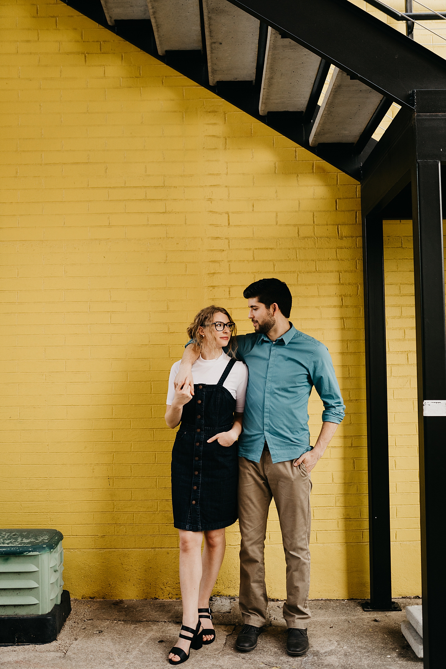 man and wife hold each other close by a yellow brick wall by Nicole Aston Photography