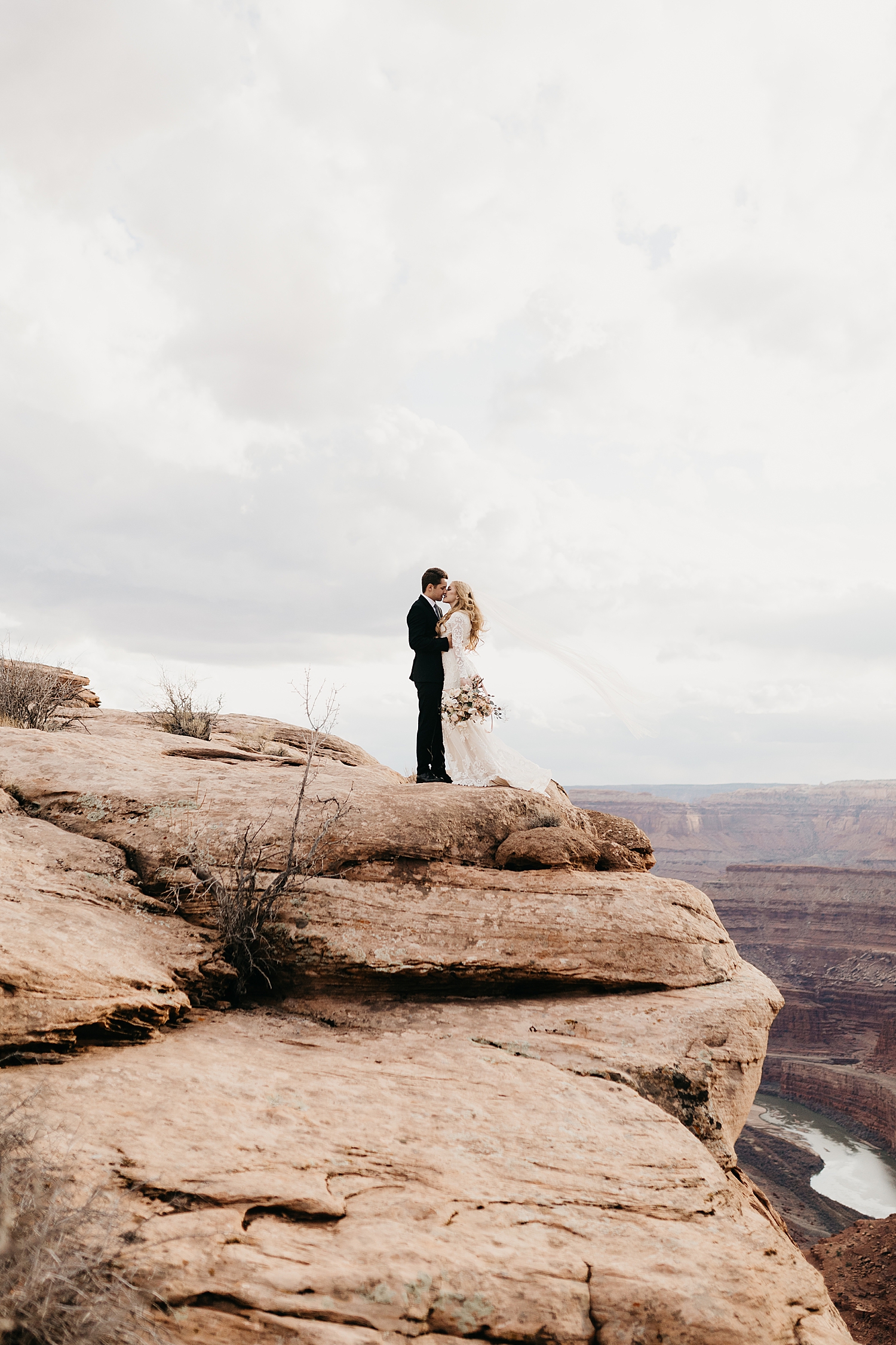 couple stand on cliffside in windy weather by Nicole Aston Photography