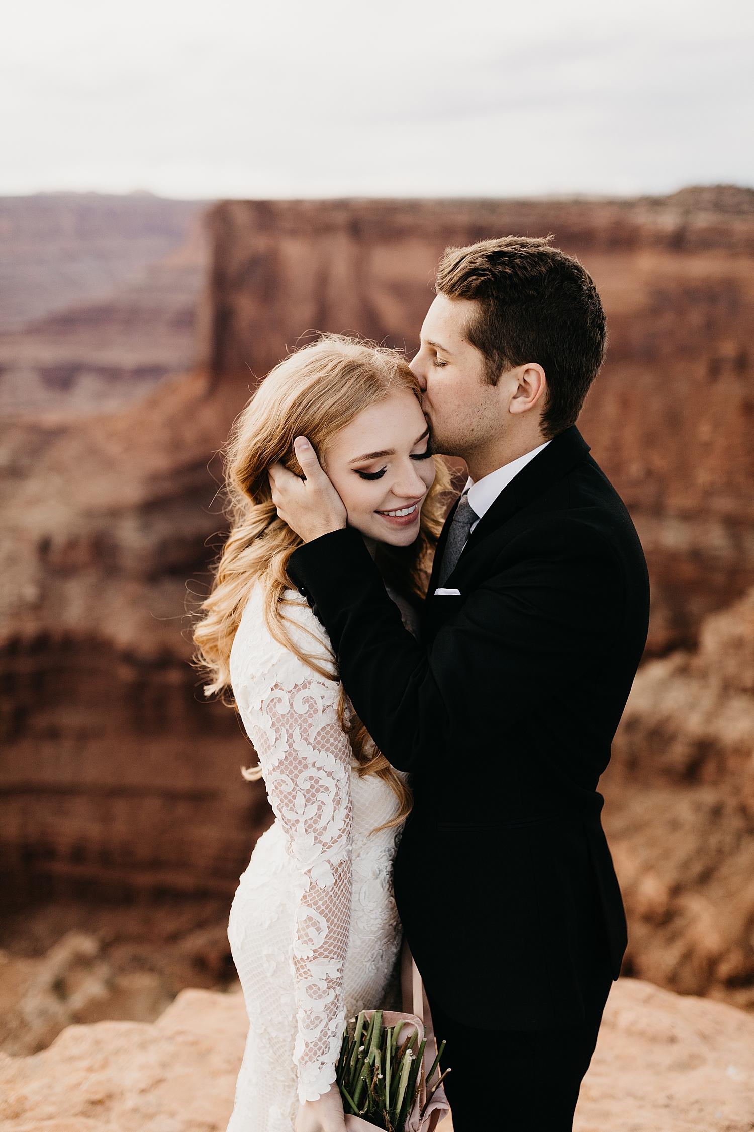 groom pulls his wife close and kisses temple during Moab Dead Horse Point Bridal Shoot