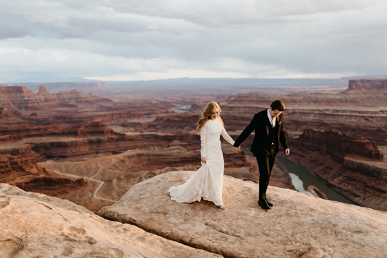 ginger bride holds husband's hand for canyon hike by Destination wedding photographer 