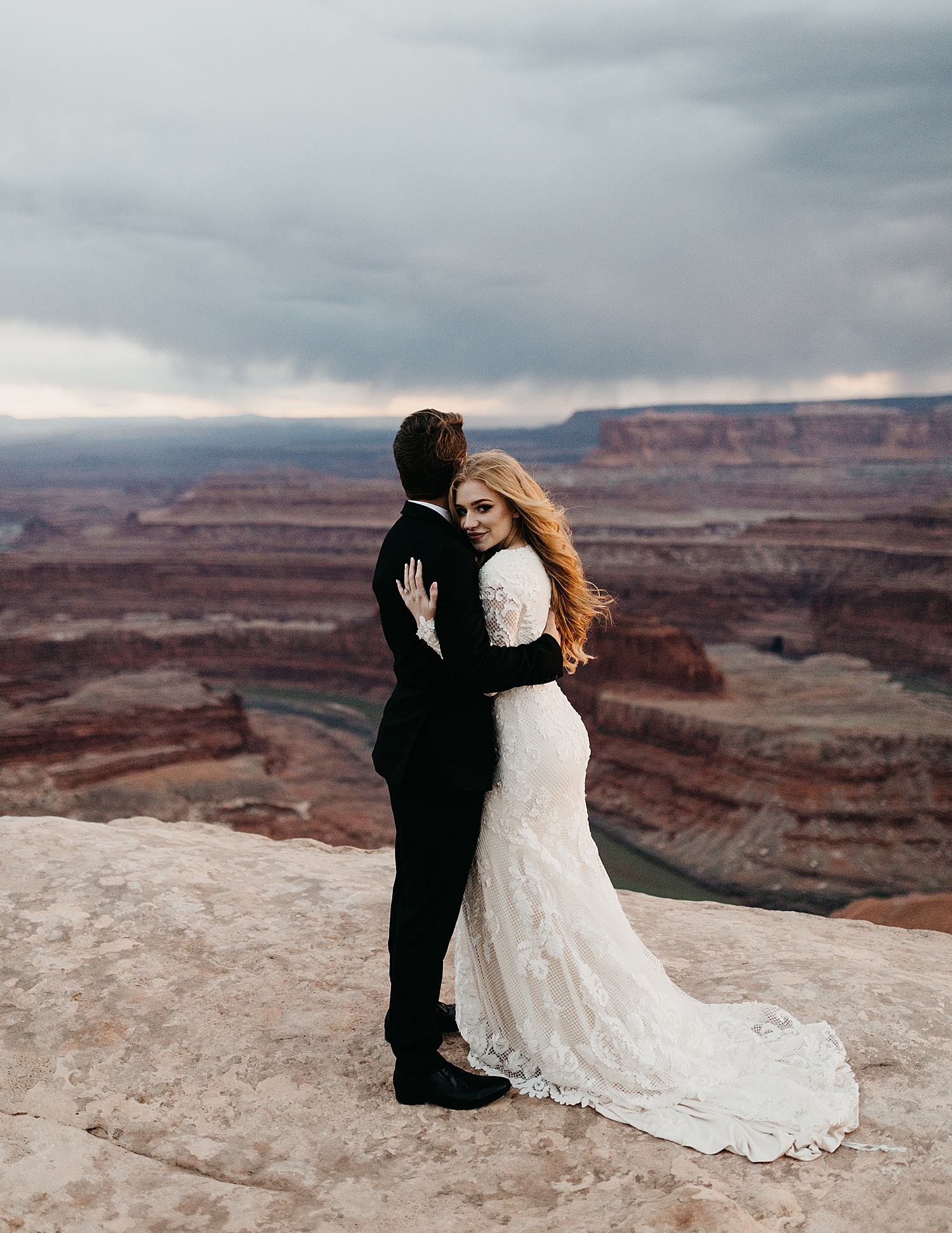 man and wife snuggle in the setting sun overlooking a canyon by Destination wedding photographer 