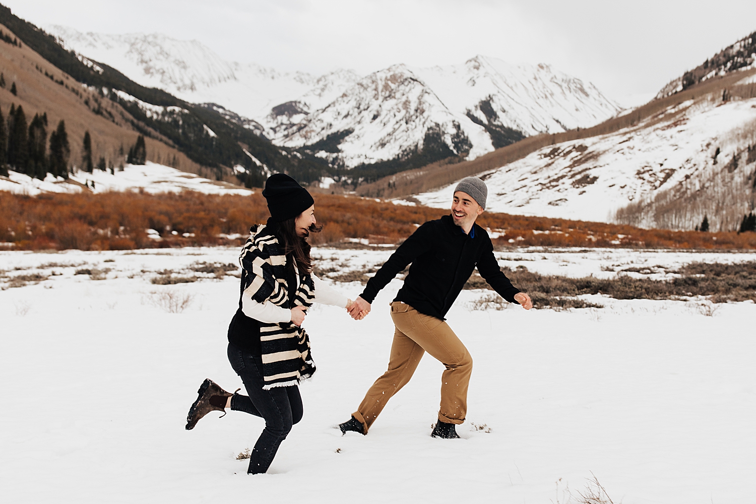 couple runs thorugh field showing 3 tips for engagement photos in the snow