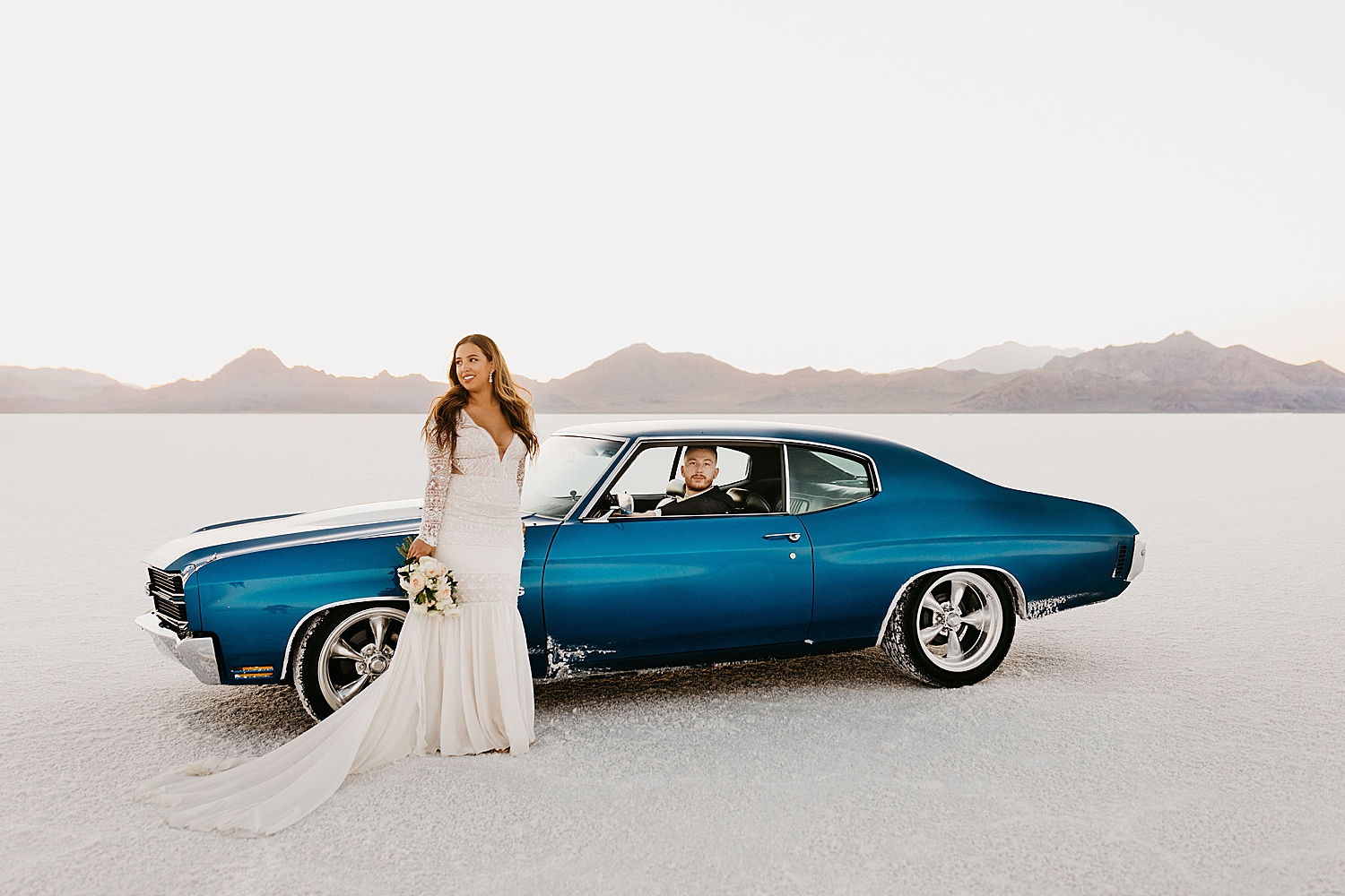 bride in full gown stands next to blue sports car by Destination wedding photographer