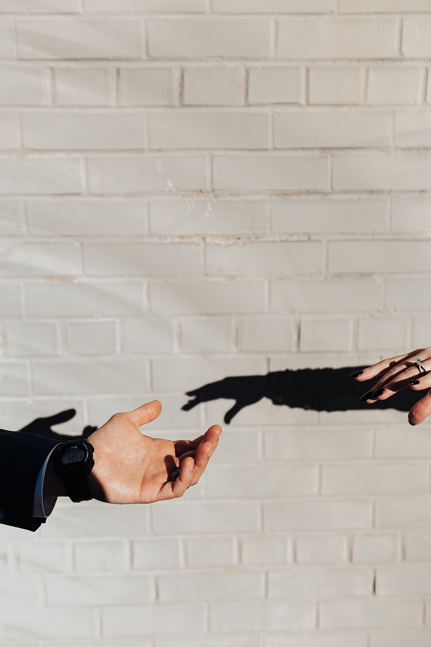 two hands reaching for each other in front of white brick wall by Destination wedding photographer