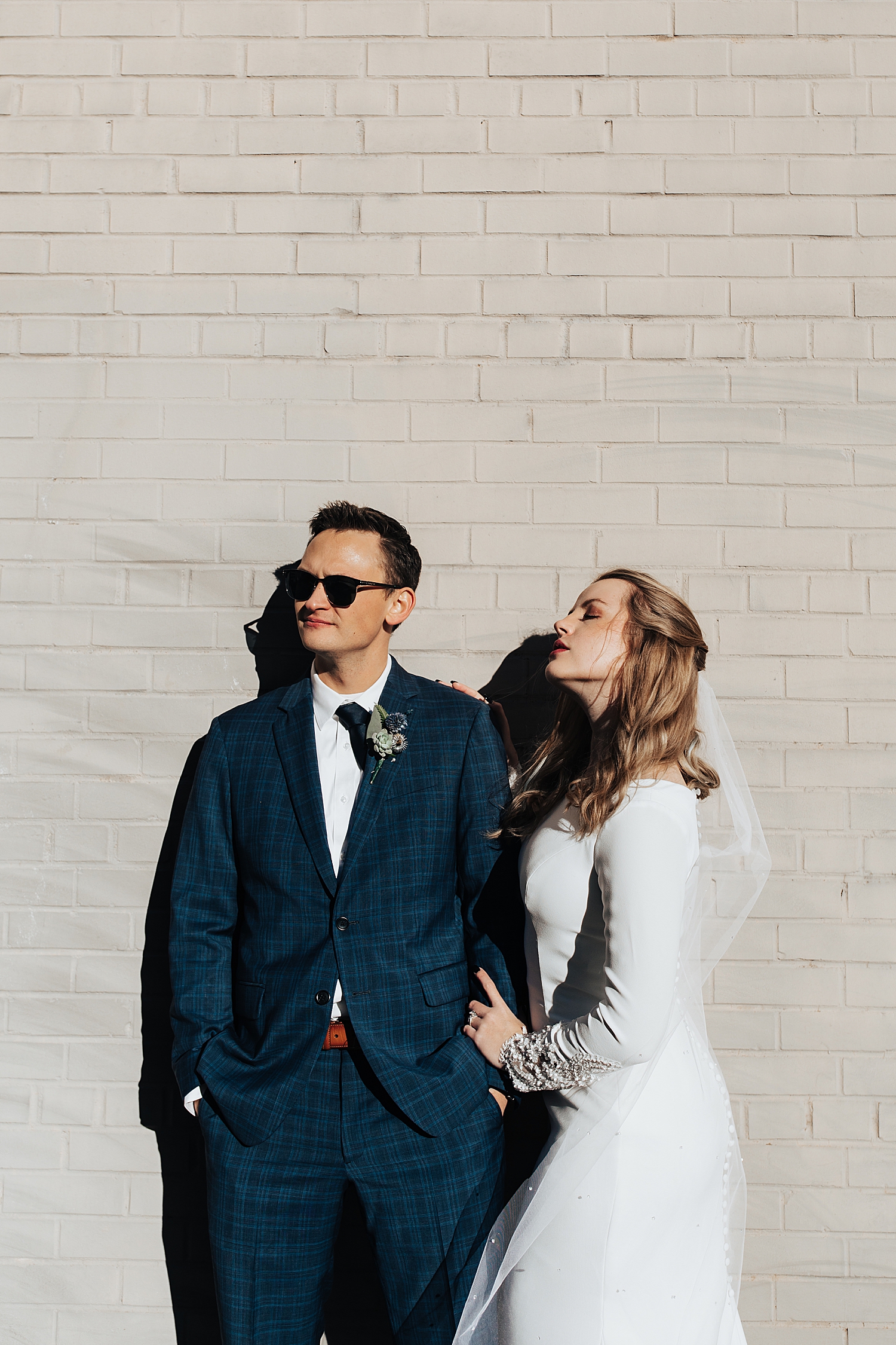 engaged couple lean against white brick wall in full sun for sunrise shoot