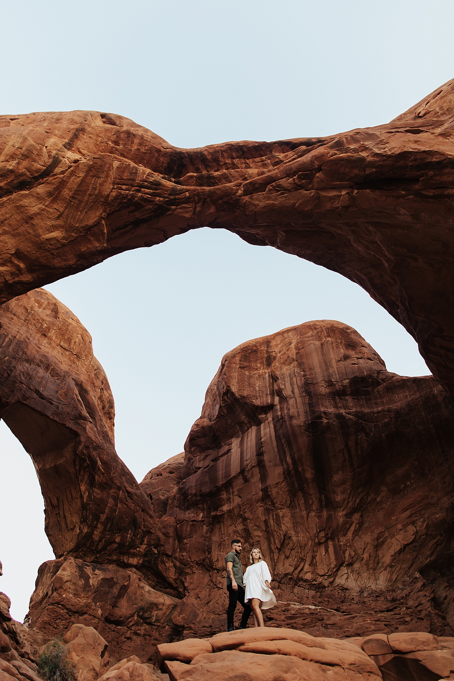woman in white dress stands next to her man under big rock by Destination wedding photographer