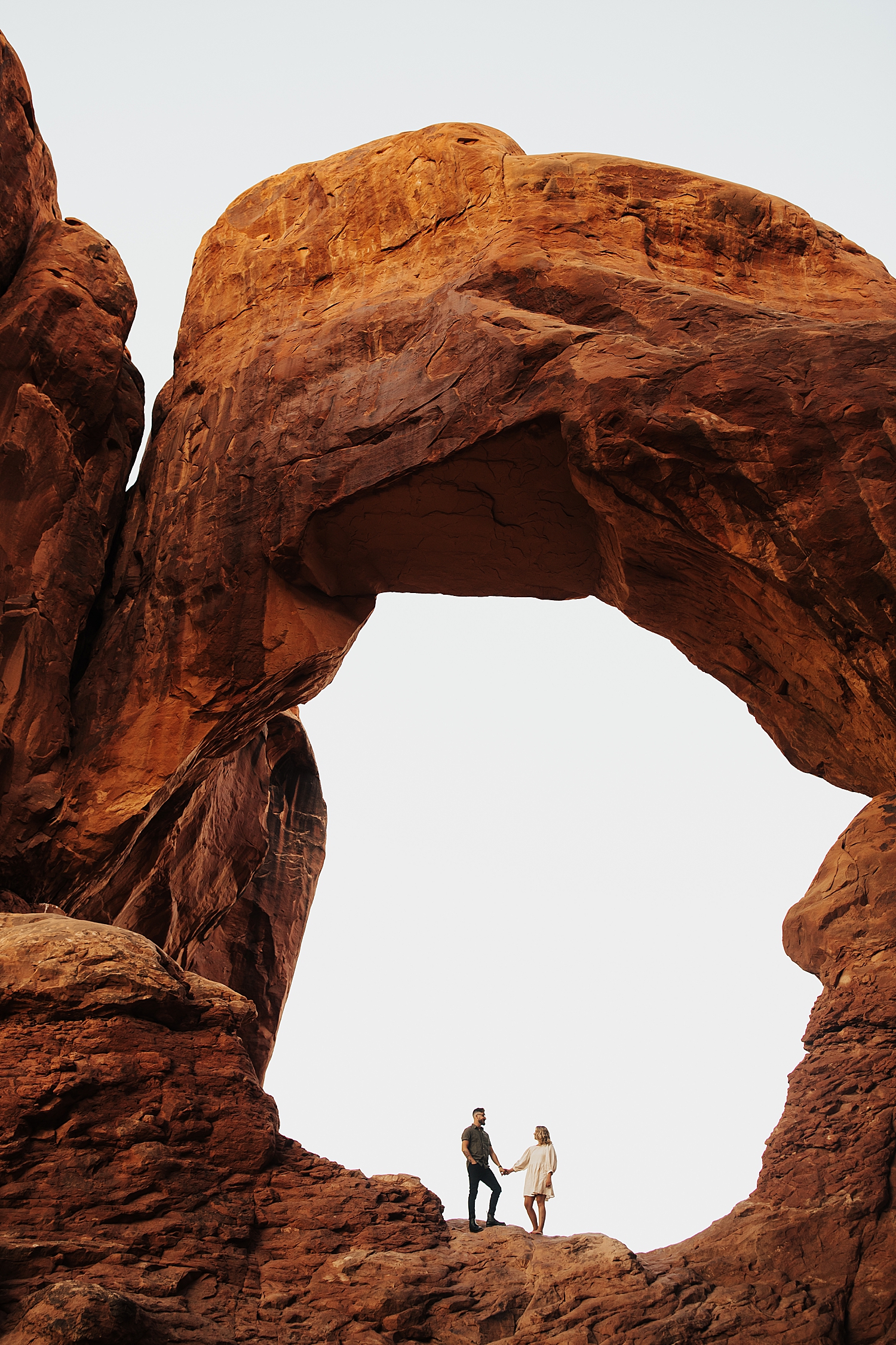 engaged couple holds hands under large stone arch by Nicole Aston Photography