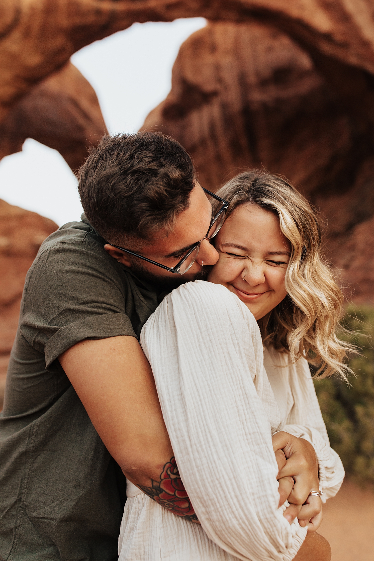 blonde woman scrunches her nose in giggle as man hugs her by Destination wedding photographer