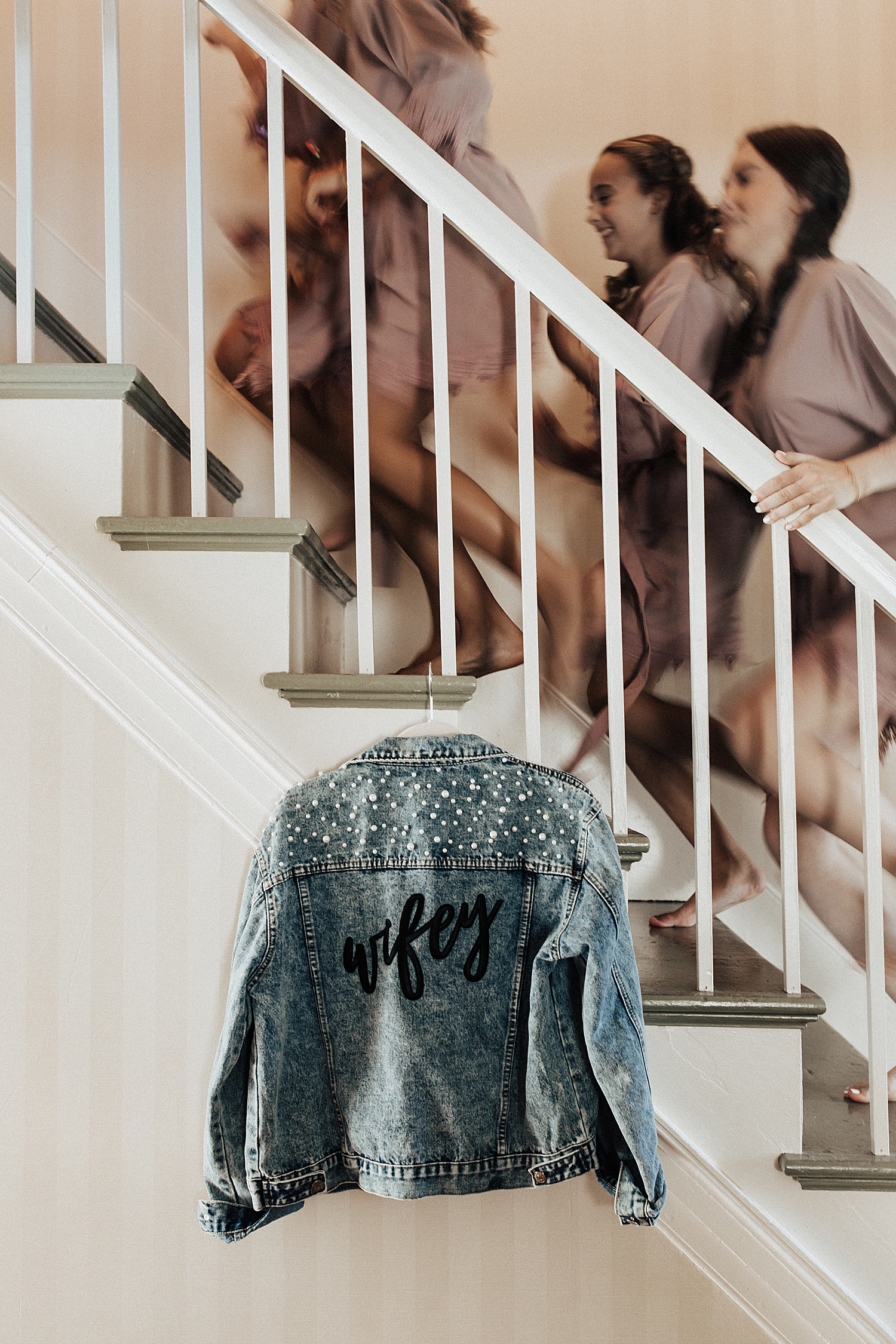 bridesmaids run up stairs with "Wifey" denim jacket hanging on railing by Nicole Aston Photography