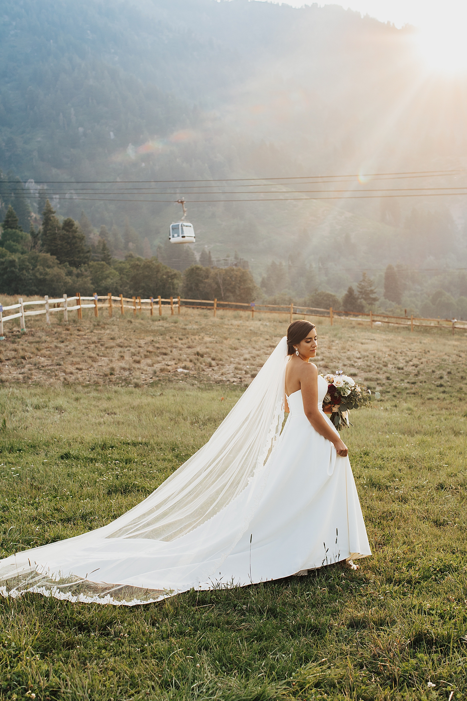 bride stands on mountainside field in sunshine by Nicole Aston Photography