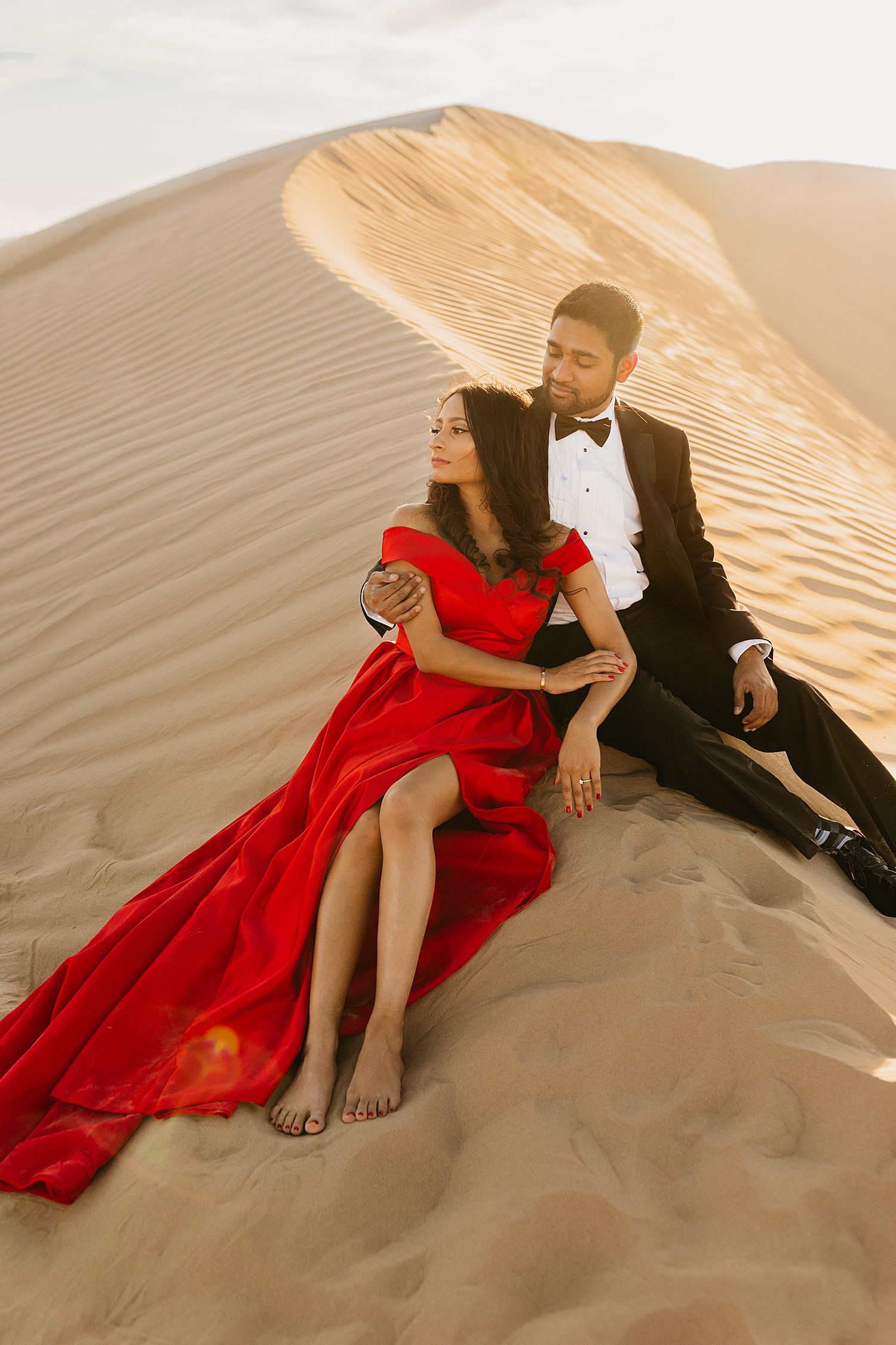 couple curl up together on the crescent ridge of a desert for Sand Dune engagement session