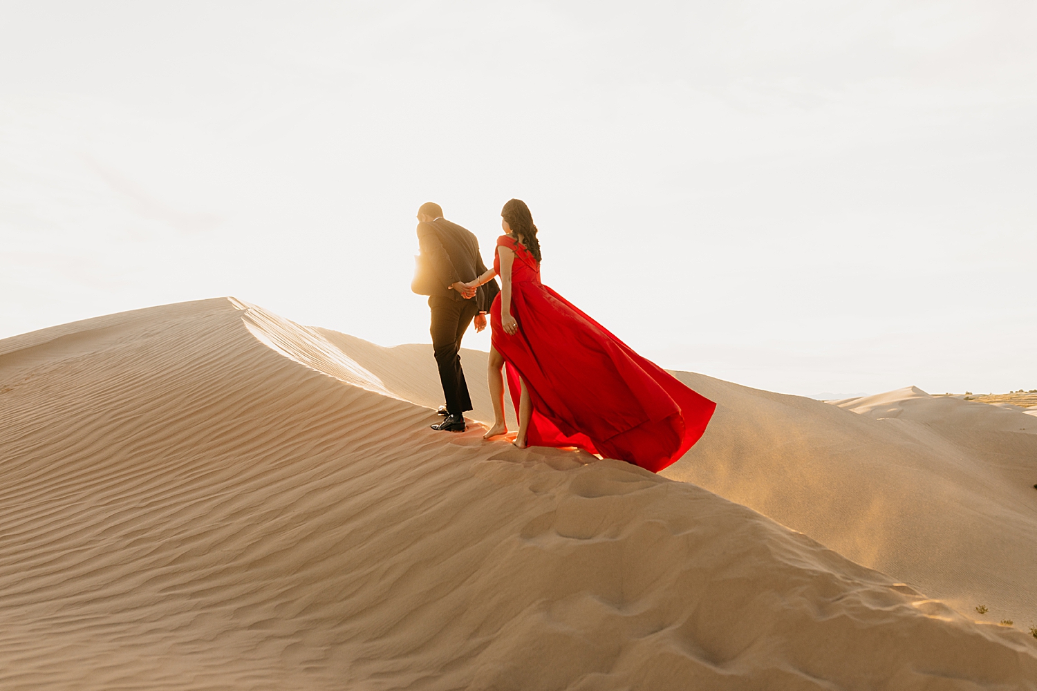 man leads woman in red dress up a hill in golden hour by Nicole Aston Photography