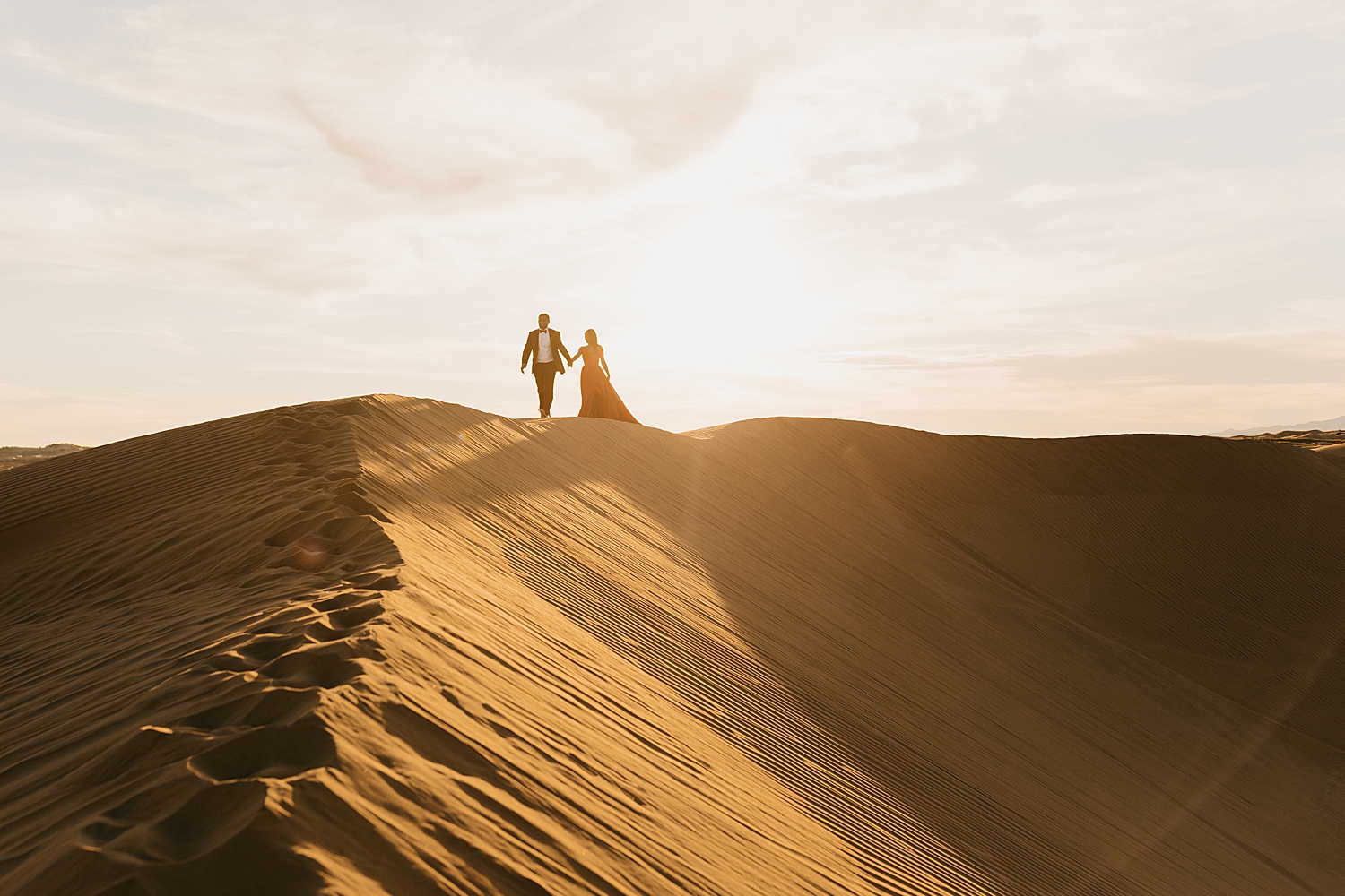 couple walks across the top of a ridge in desert during golden hour by Nicole Aston Photography