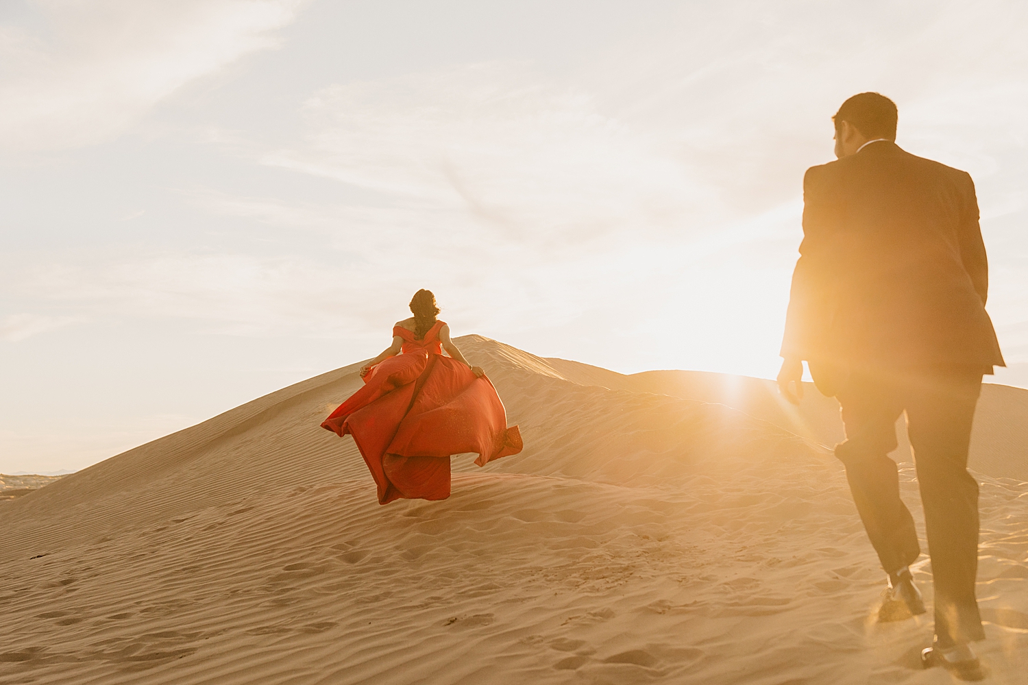 woman in red ballgown races up hill for Sand Dune engagement session