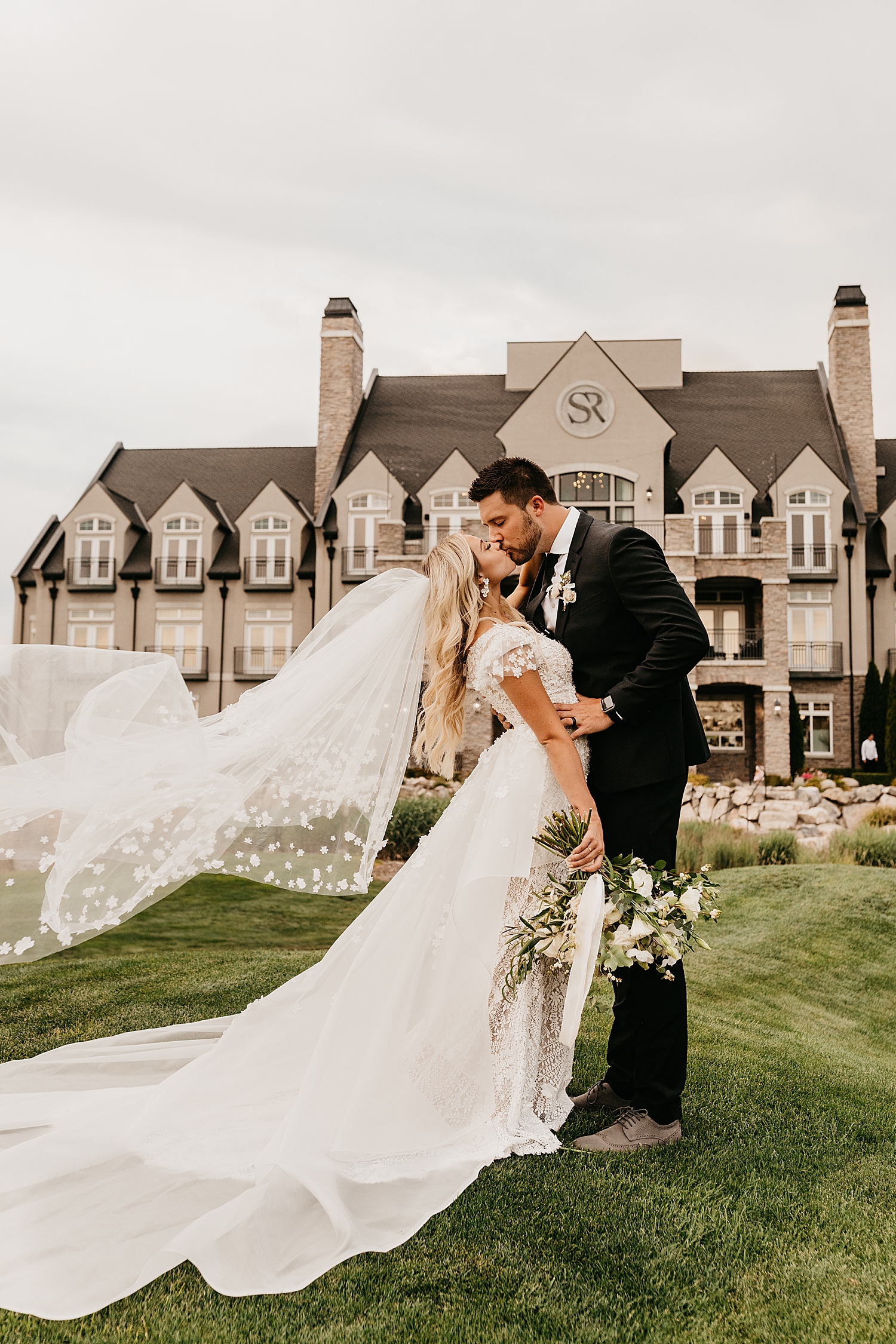newlyweds stand in front of large manor, Sleepy Ridge with wind blowing