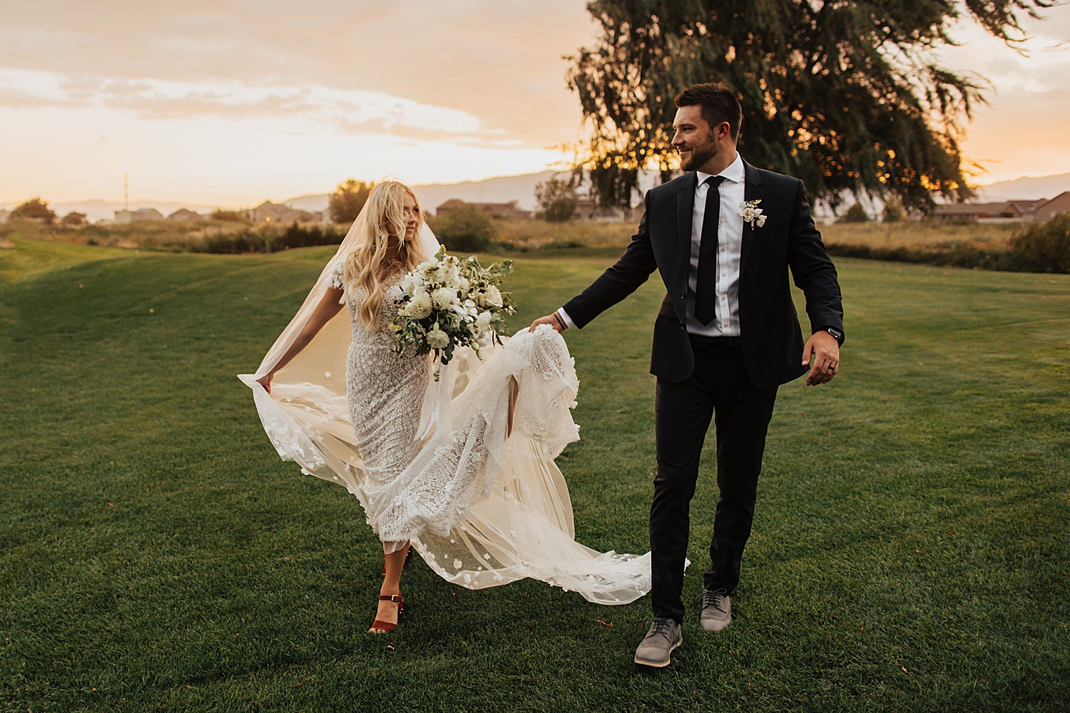 husband and wife walking across field in golden hour by Destination wedding photographer
