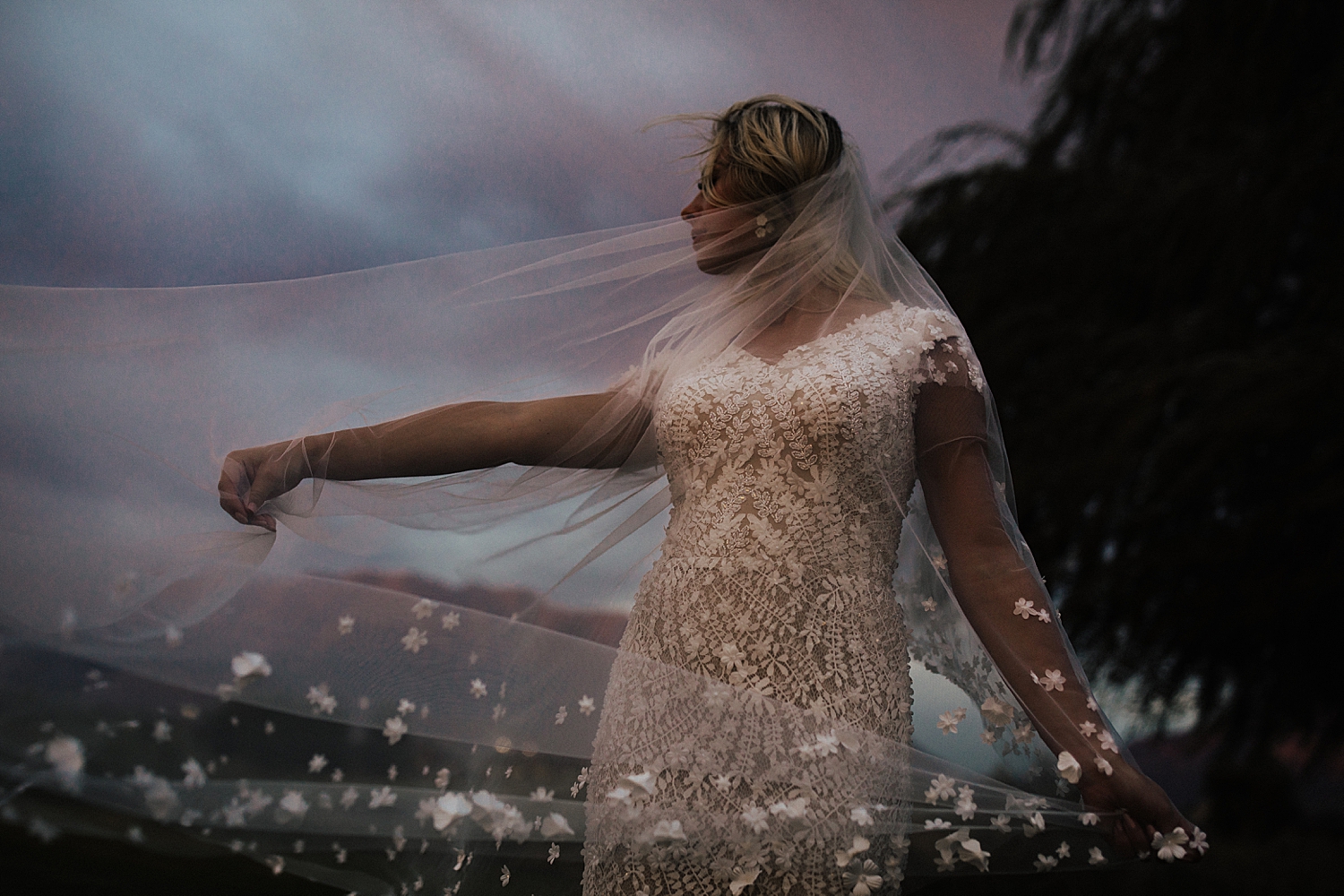 bride stands wrapped in veil under blue fading light by Destination wedding photographer