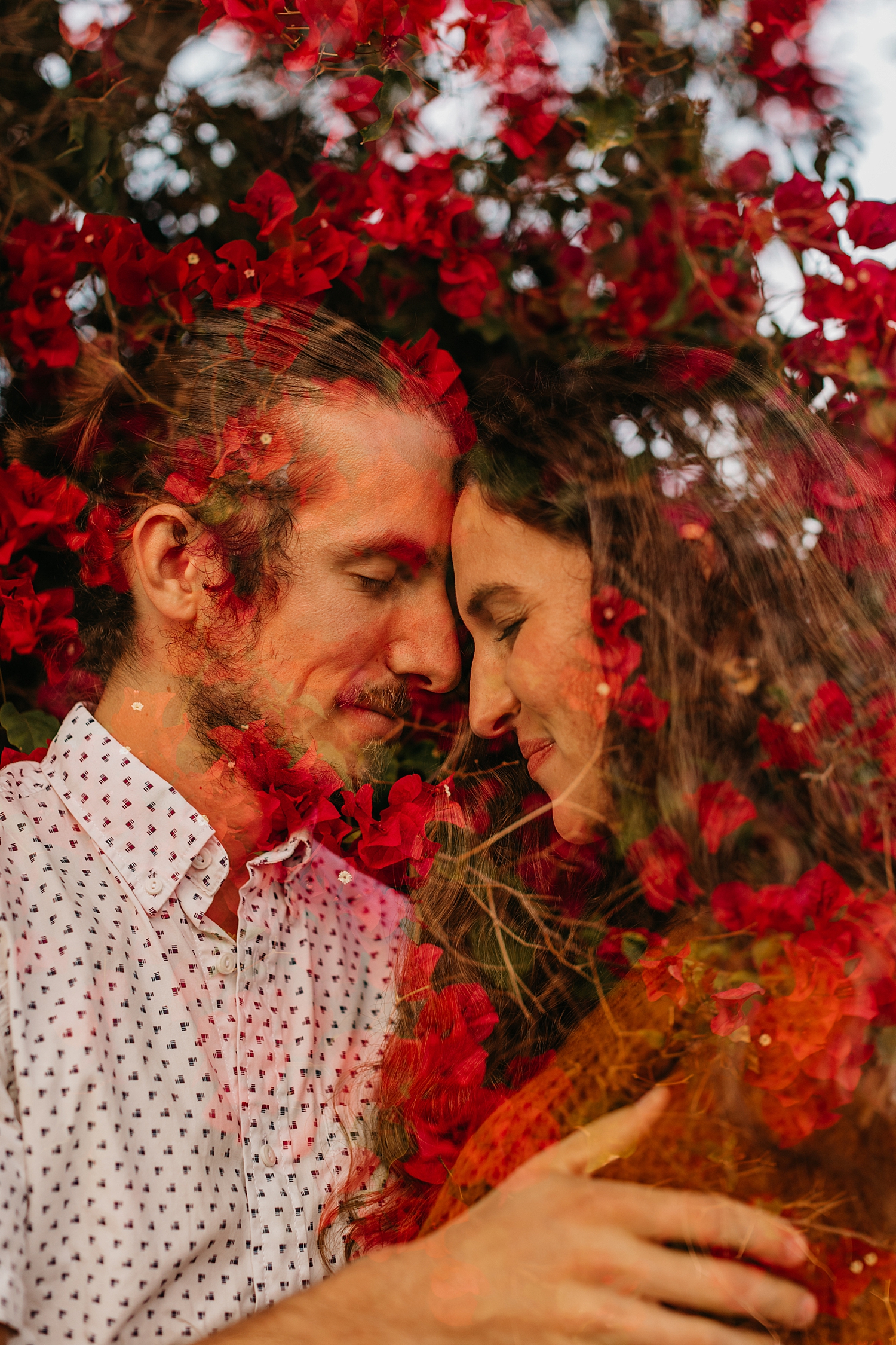 couple leans their foreheads together under red flowers by Destination wedding photographer