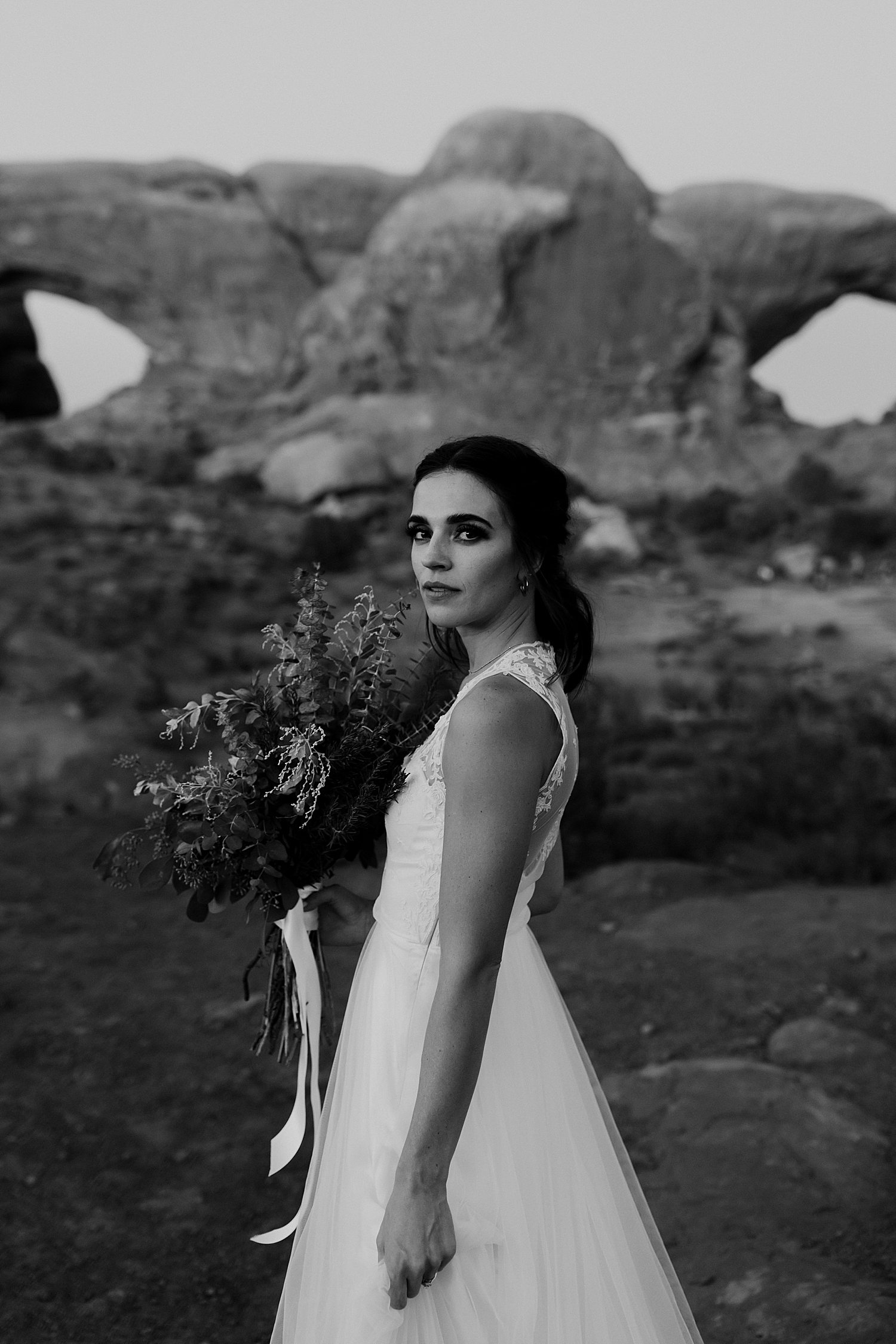 brunetter bride holds flowers with arches behind her for Moab wedding portraits
