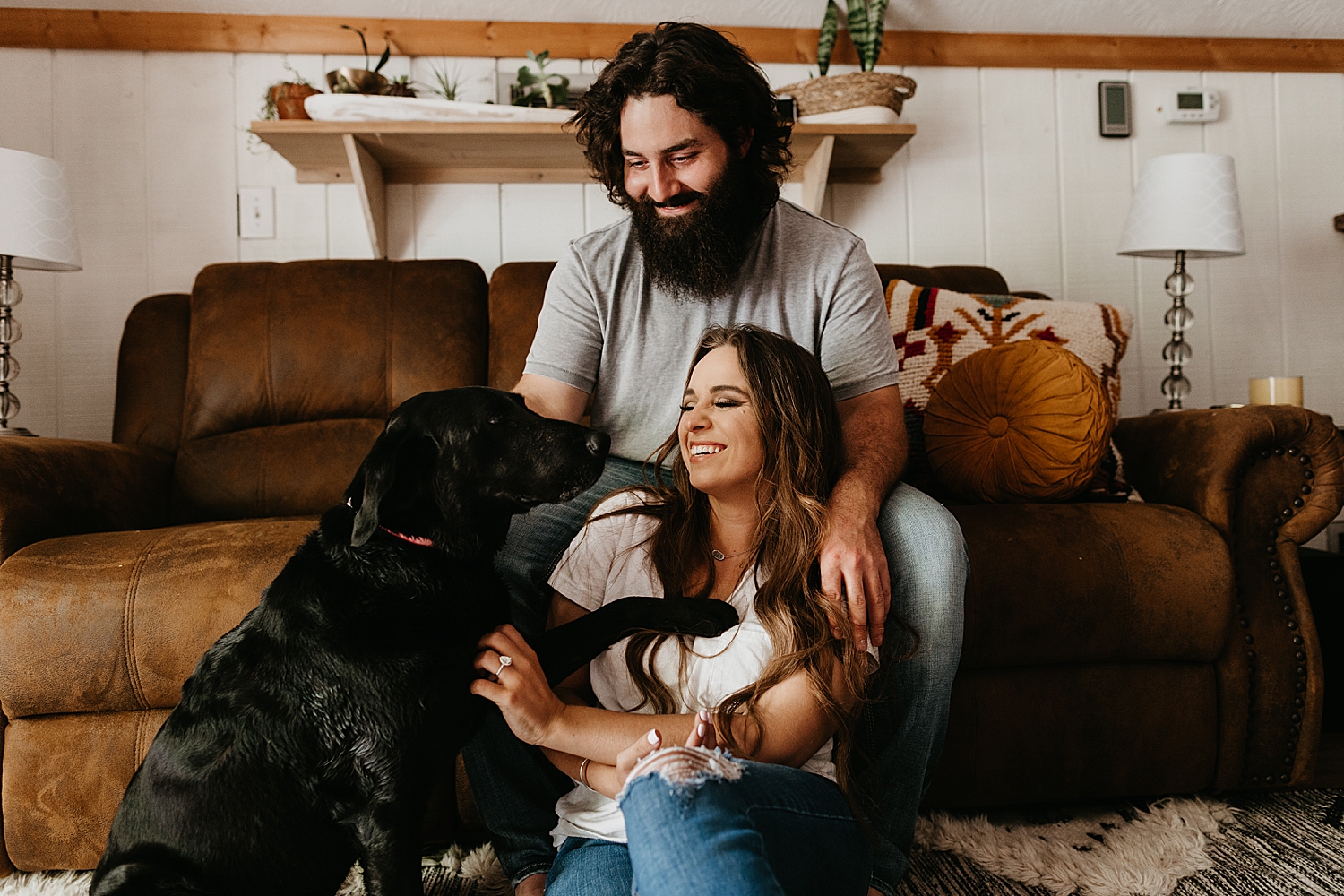 couple play with their dog on couch for in-home engagement session