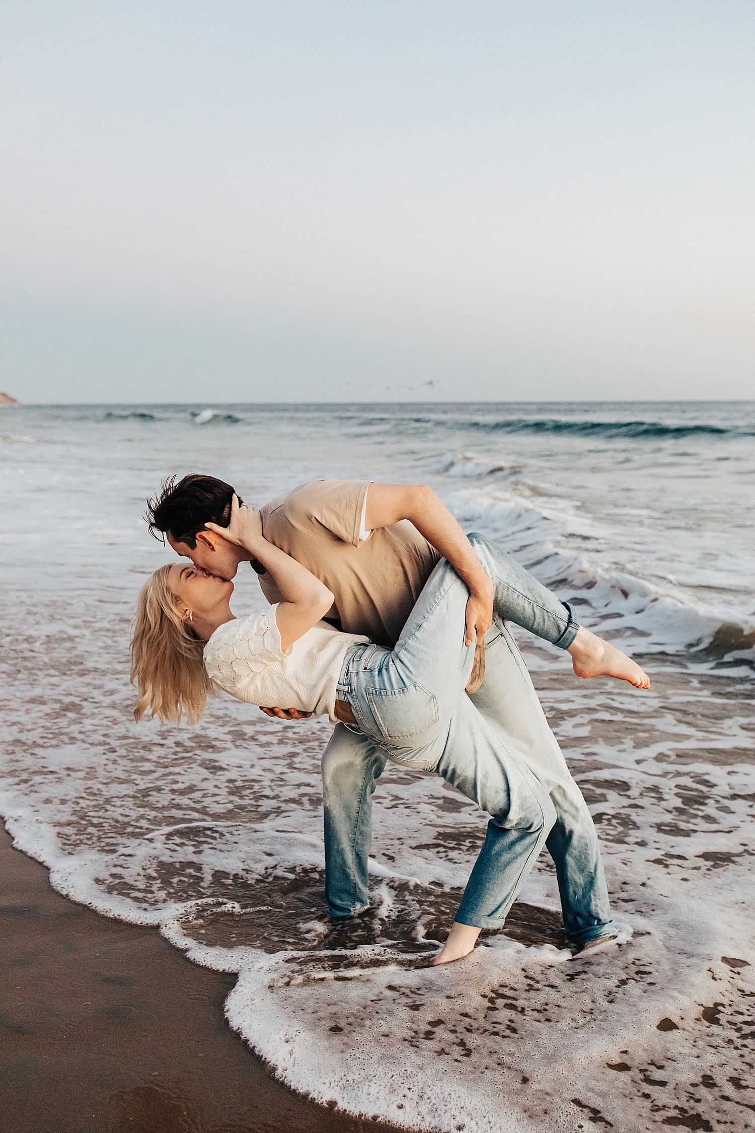 groom dips his wife-to-be in the ocean showing 10 Tips for Nailing Your Engagement Session