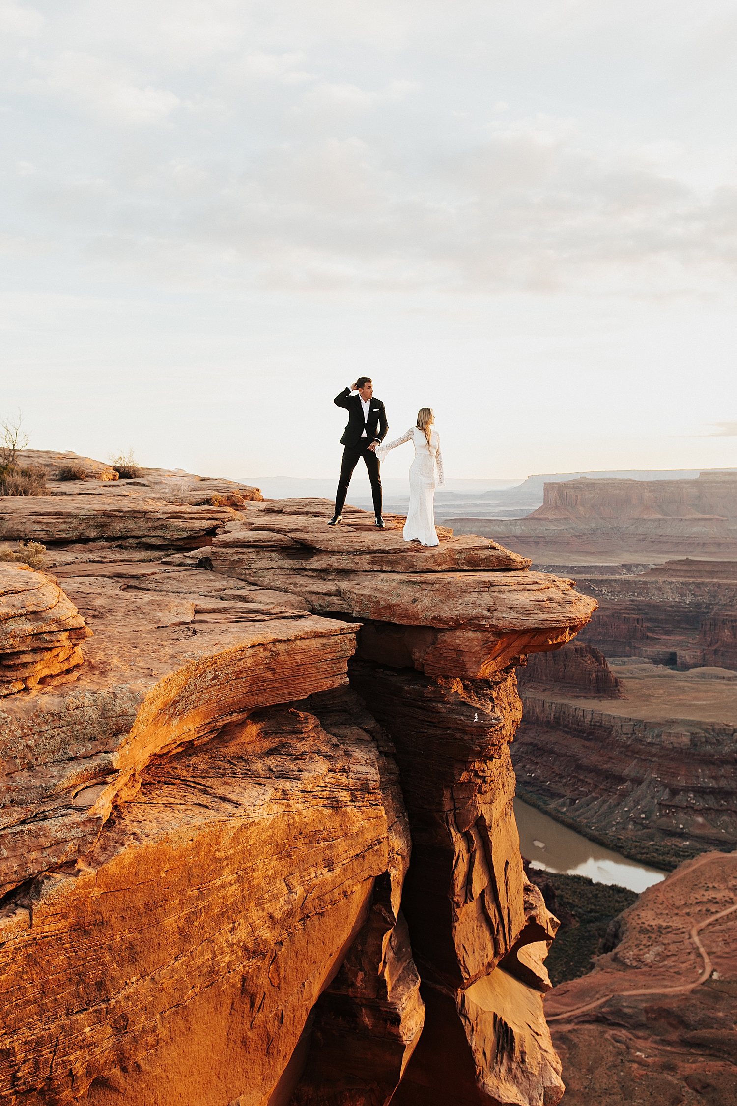 newlyweds stand on cliffside overlooking canyon by Destination wedding photographer