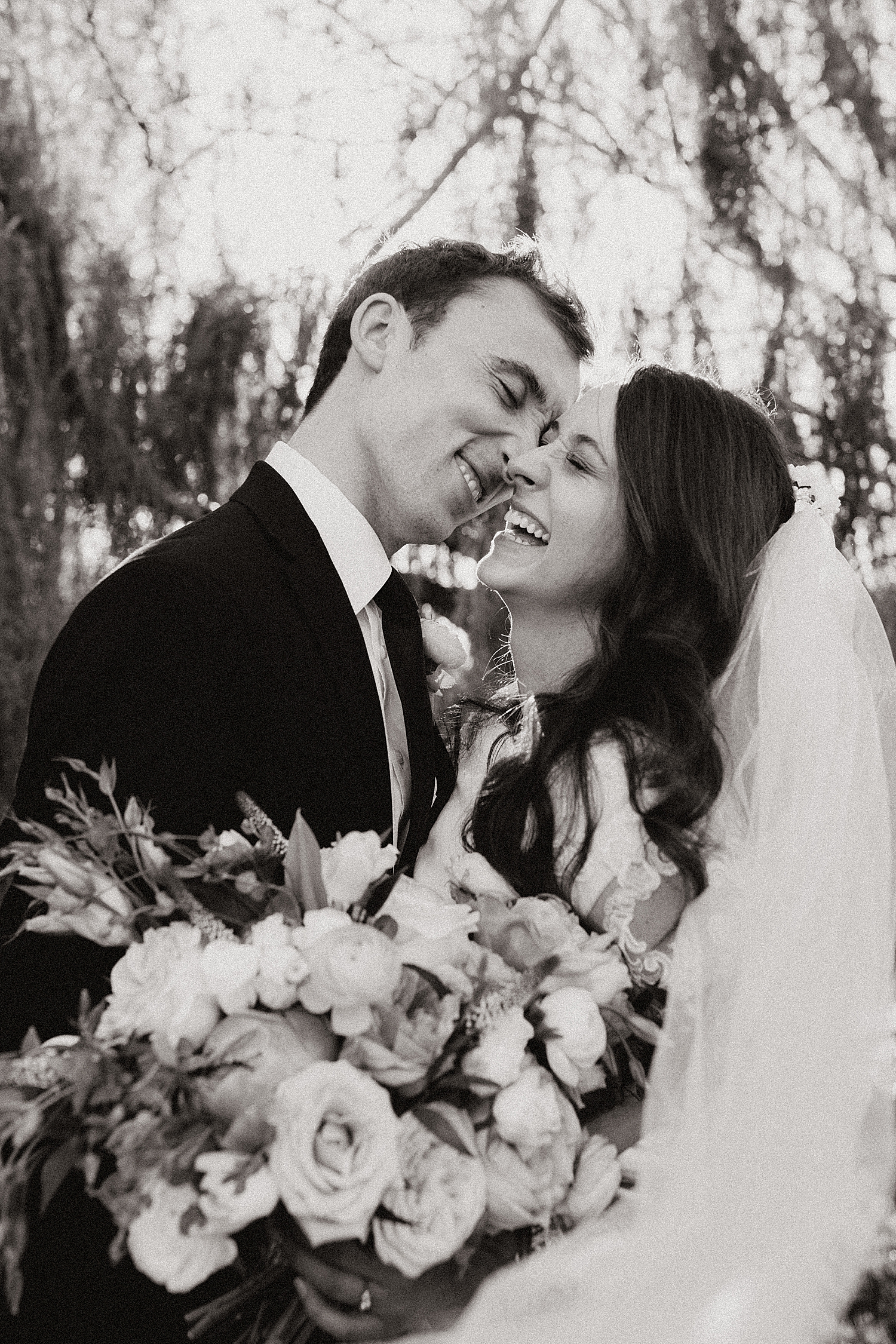 bride laughs as man leans down to kiss her for blossom bridal session