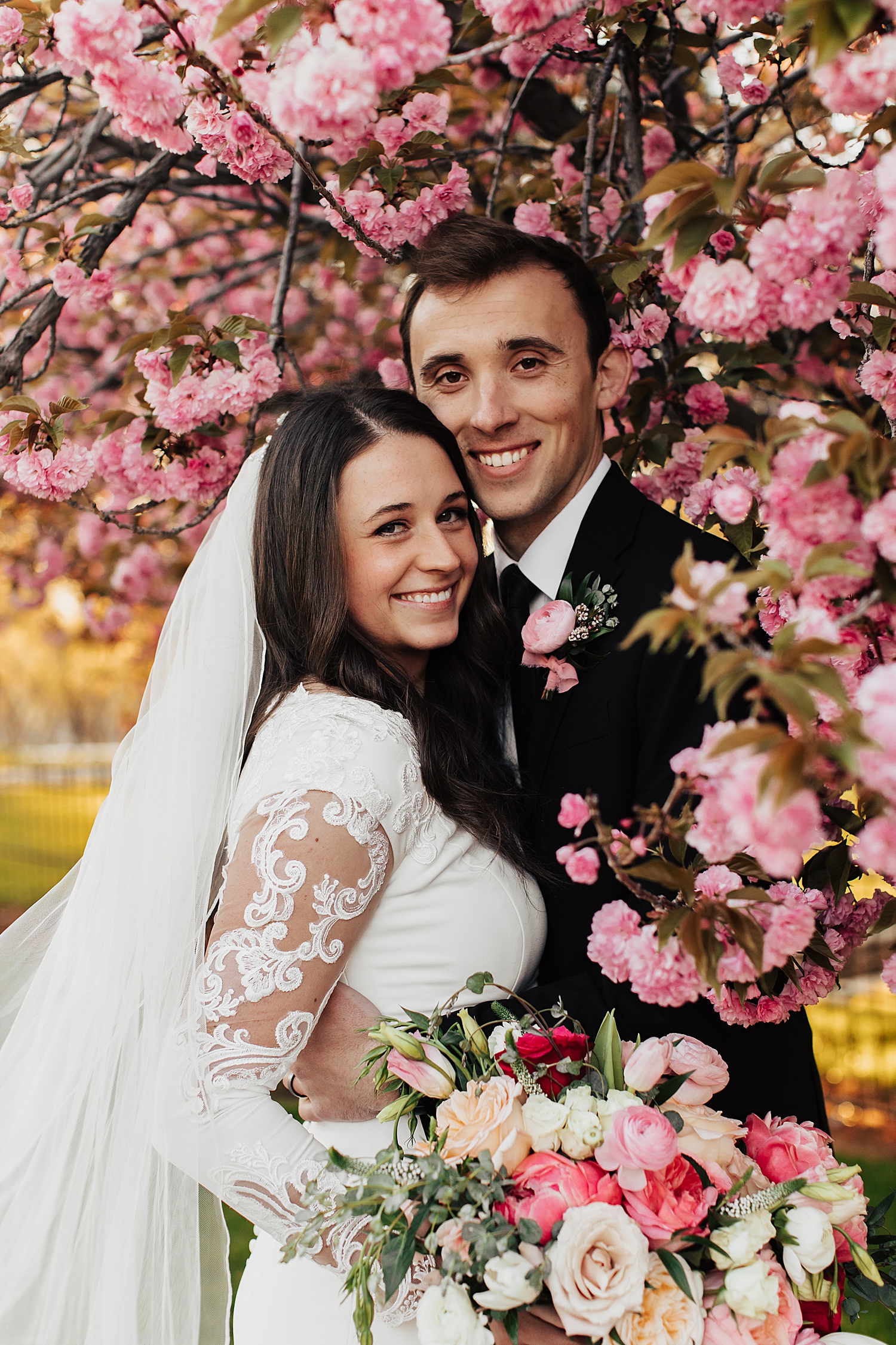 brunette couple embrace amidst flowers for blossom bridal session