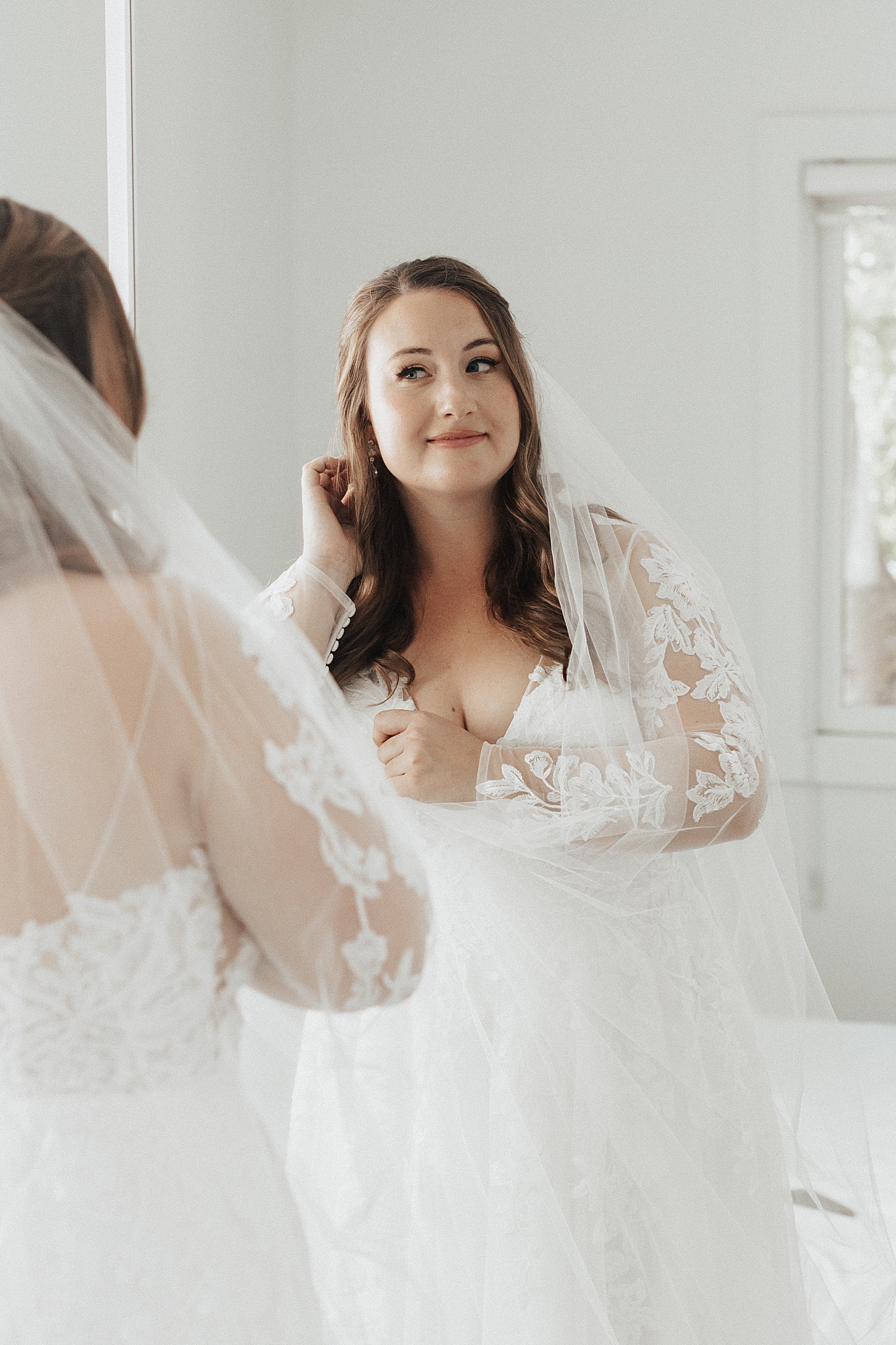 bride-to-be adjusts earrings in mirror by Nicole Aston Photography