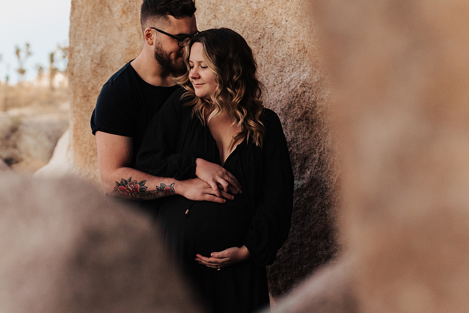 husband kisses wife's temple while holding her bump for Maternity Photos at Joshua Tree