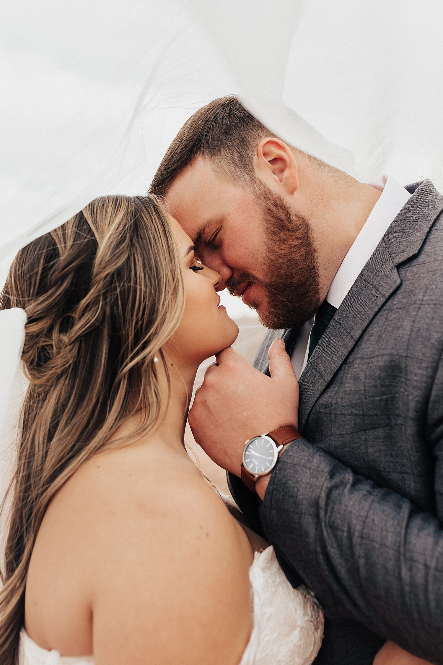 husband tips wife chin up for kiss under a veil at Snow Canyon