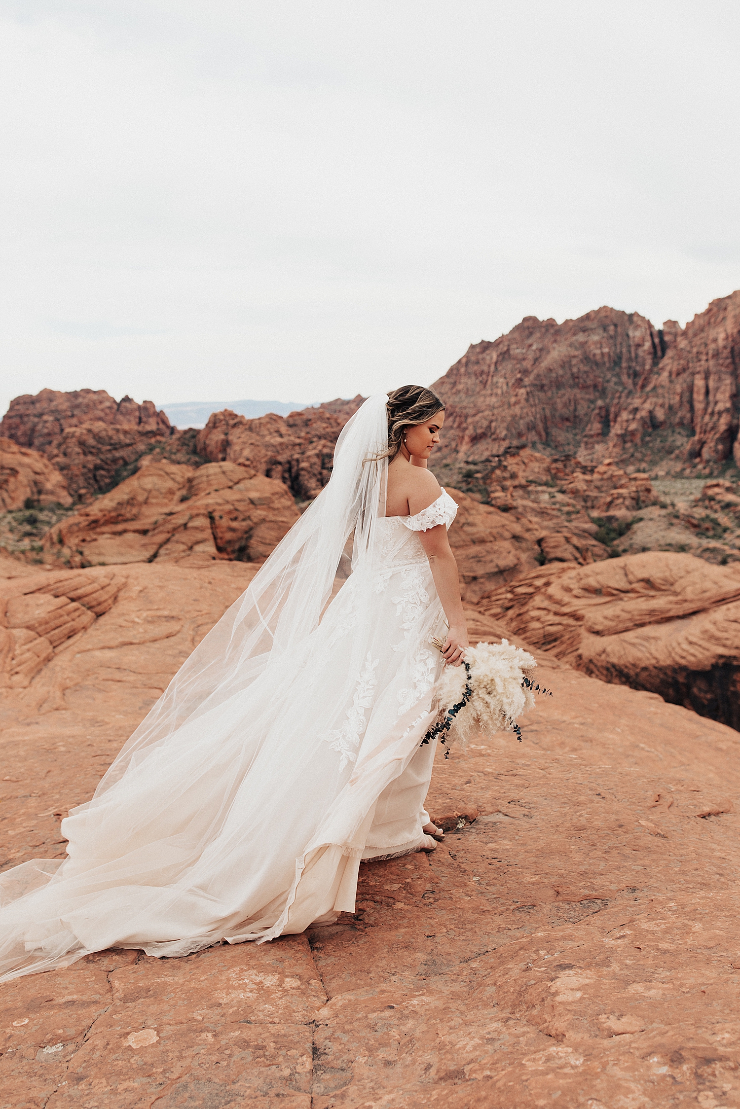 brides stands on large rock with veil blowing in the wind by Destination wedding photographer