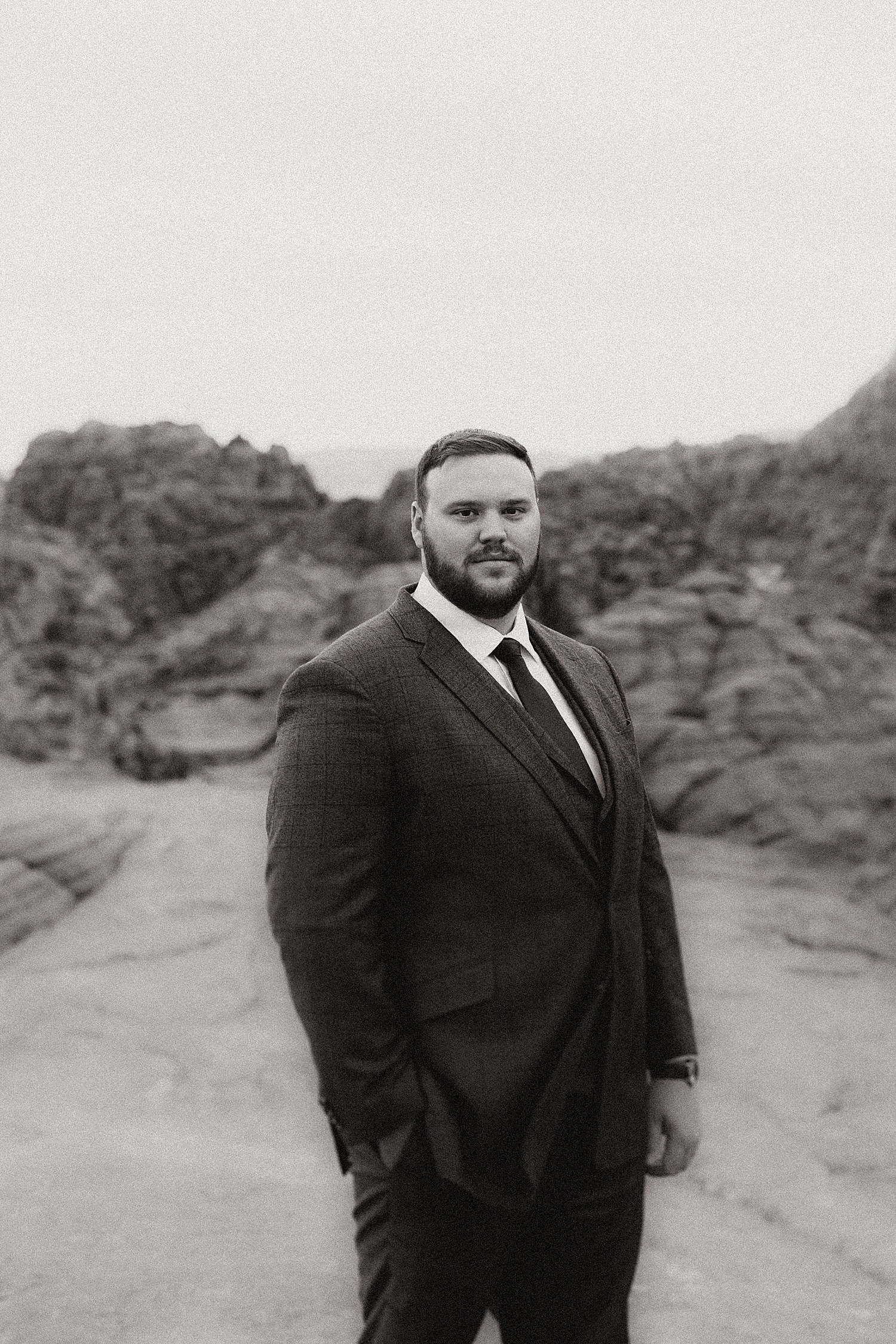 groom in suit stands in desert landscape by Nicole Aston Photography