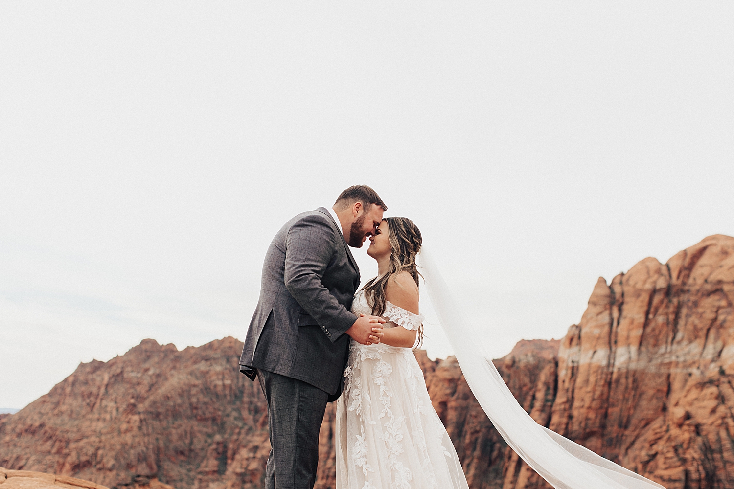 newlyweds embrace with red rocks behind them at Snow Canyon