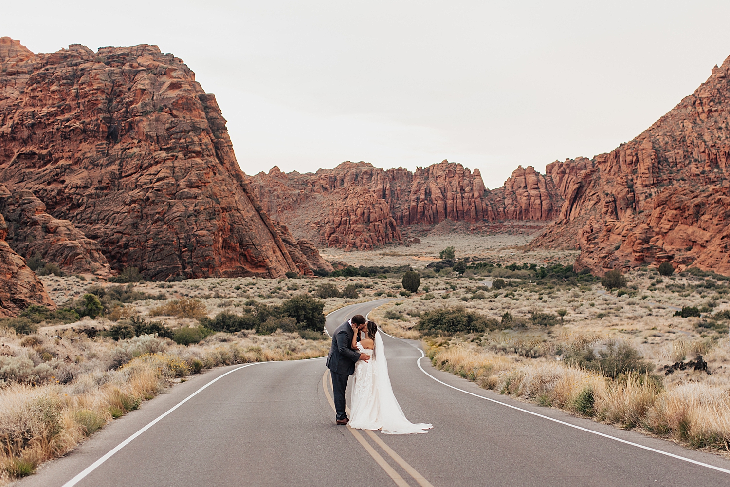 man and woman kiss on winding street in Snow Canyon by Nicole Aston Photography
