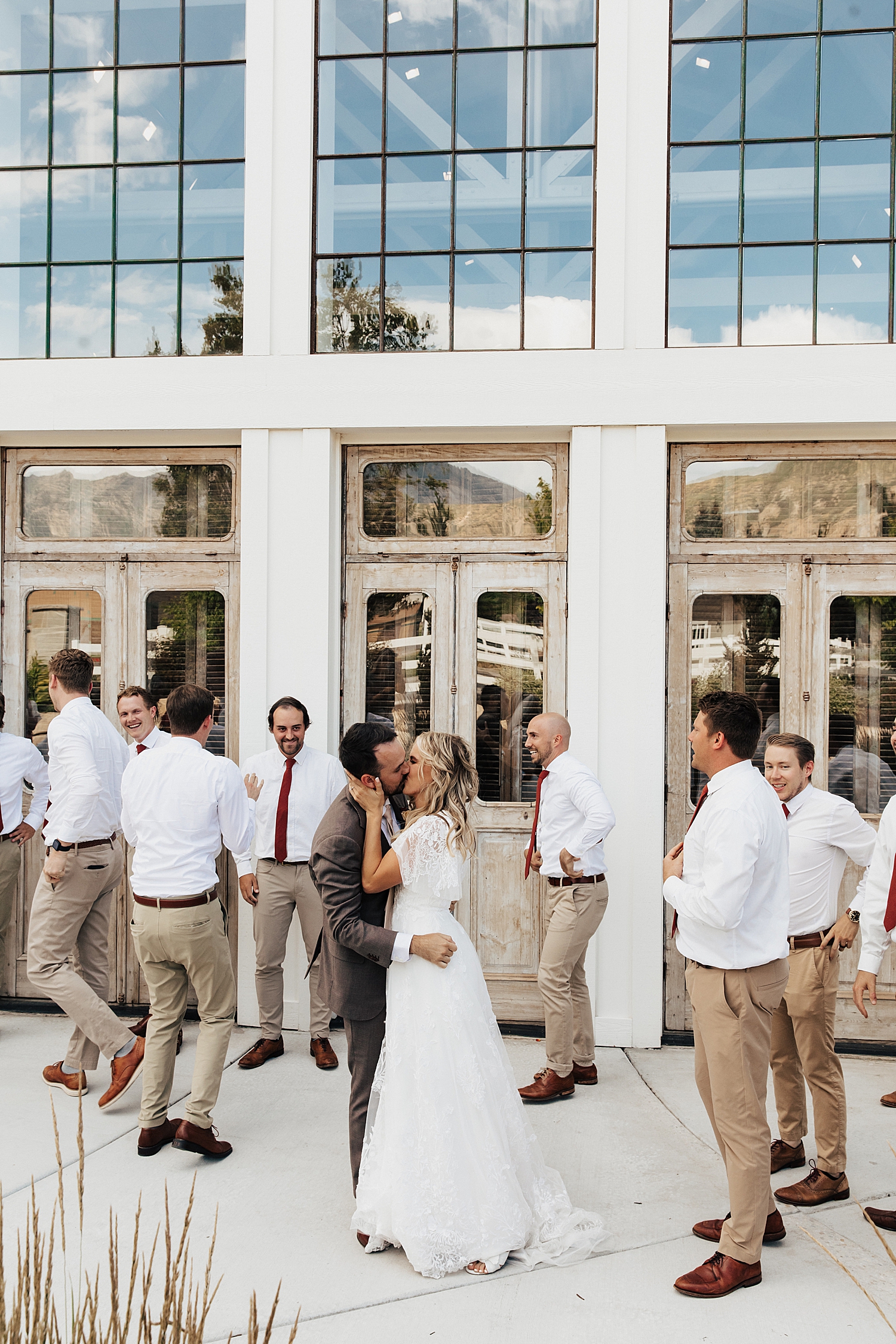newlyweds share a kiss while groomsmen walk past by Destination wedding photographer