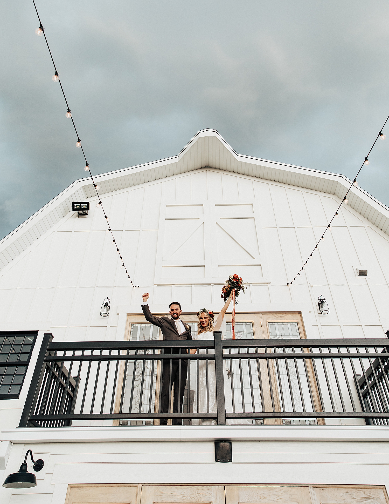 newlyweds stand on balcony waving to guests below by Nicole Aston Photography