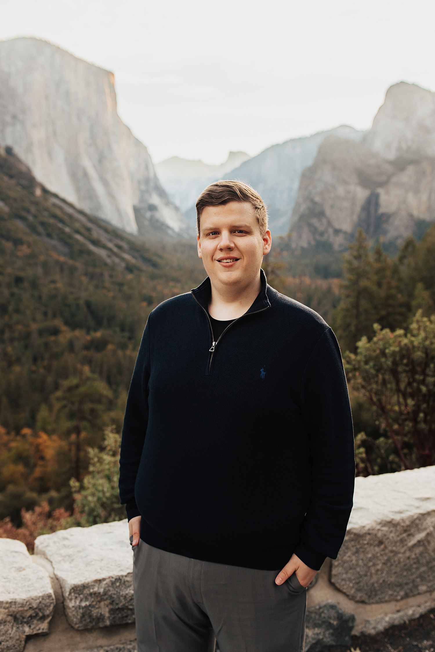 man in black half zip stands with mountains in the background for Yosemite engagement session