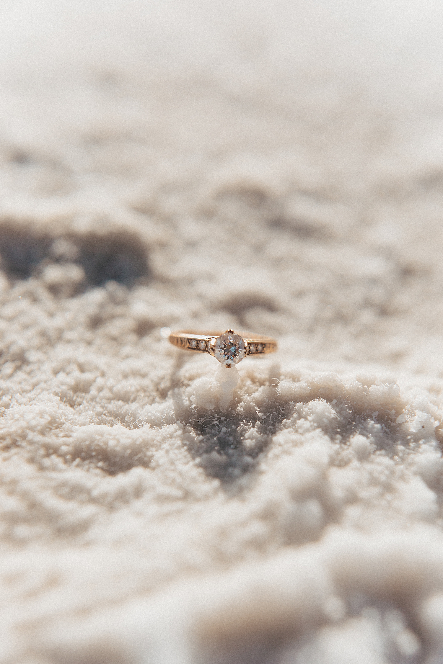 small diamond and gold ring sitting in bed of natural salt by Destination wedding photographer
