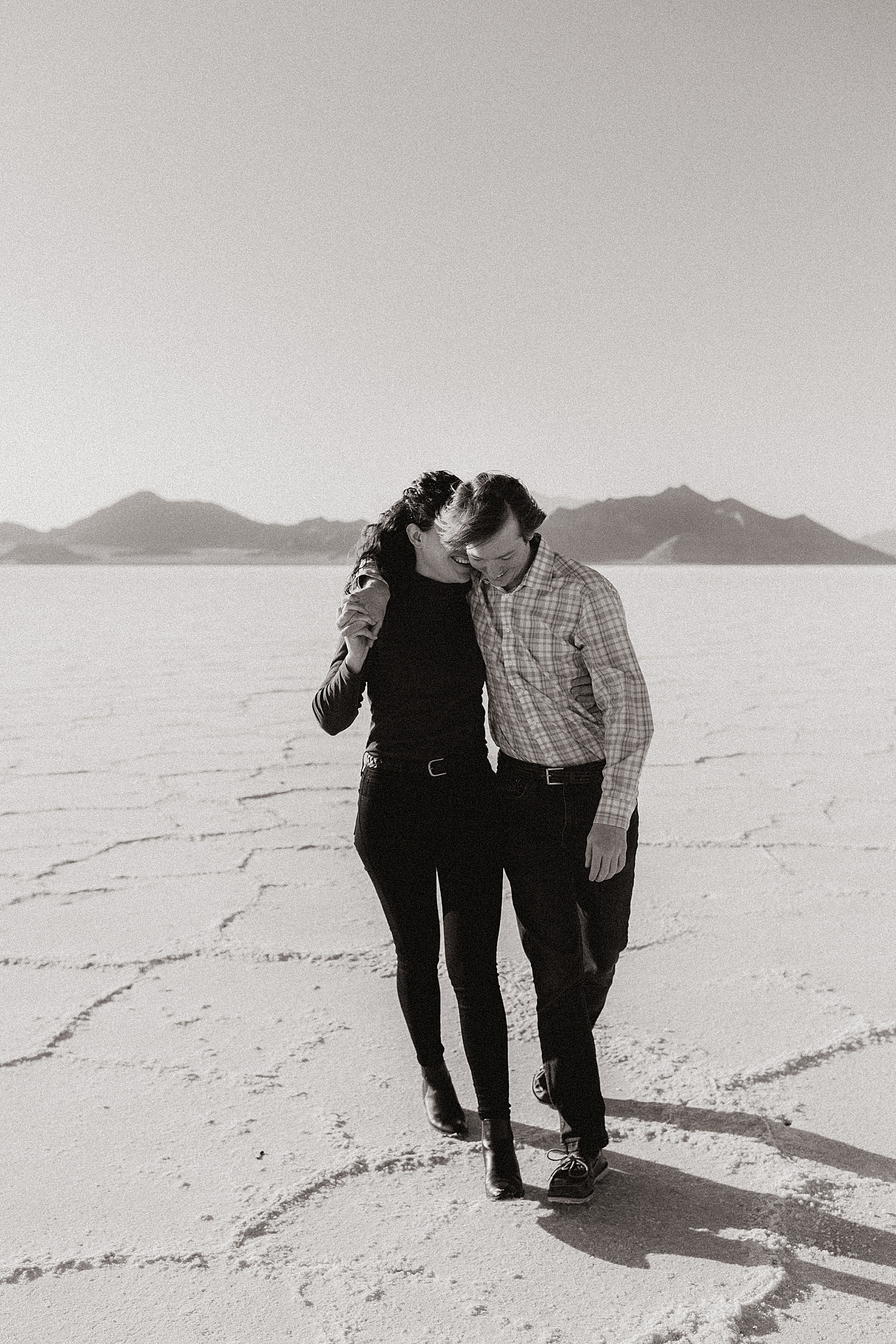 couple walks arm in arm laughing together across desert by Nicole Aston Photography