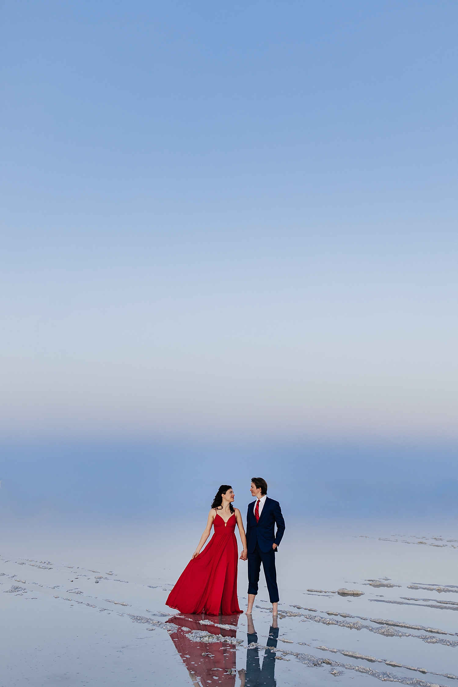 man in suit stands with woman in red dress on the flooded salt flats