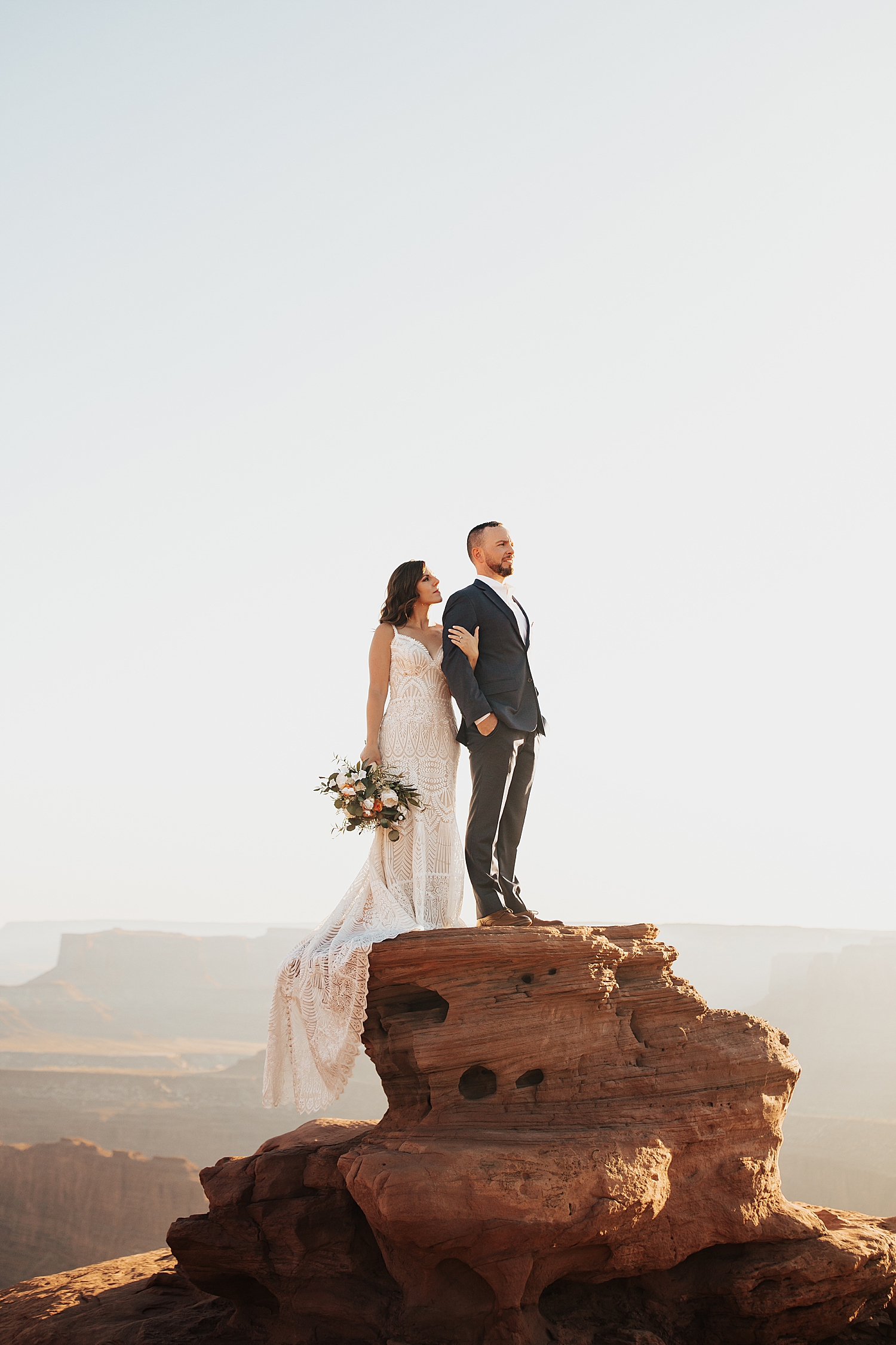 man and woman stand on oversized rock overlooking dead horse point by Destination elopement photographer