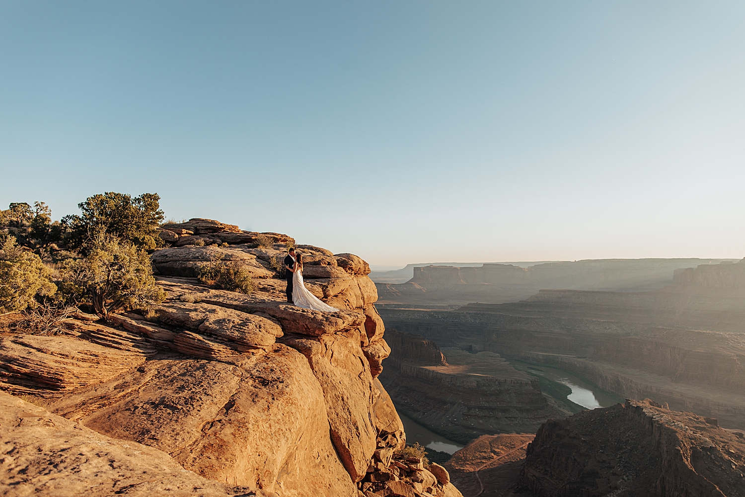 couple embrace on large red rock overlooking canyon by Nicole Aston Photography