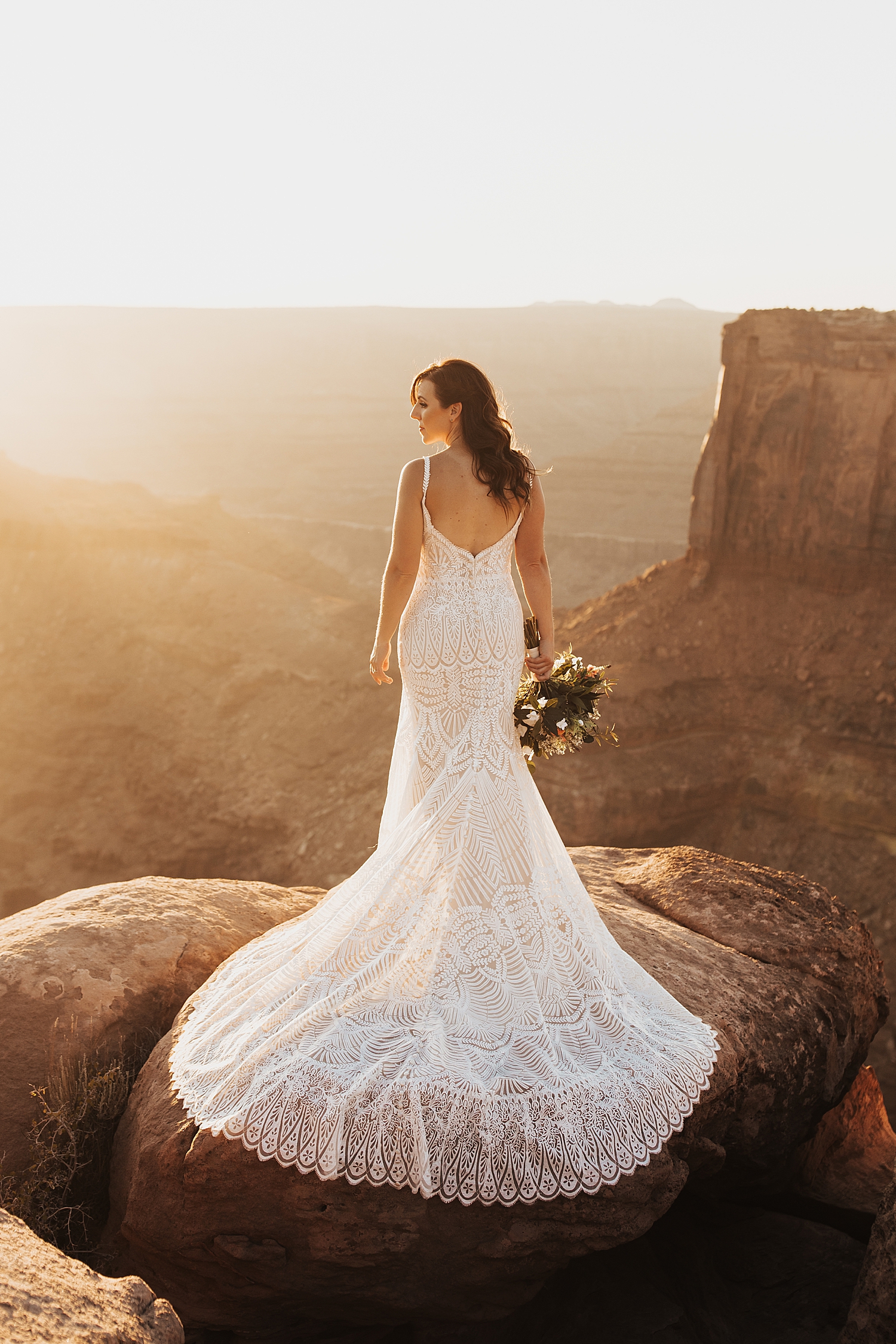 brunette woman in long lace white dress stands on a rock by Nicole Aston Photography